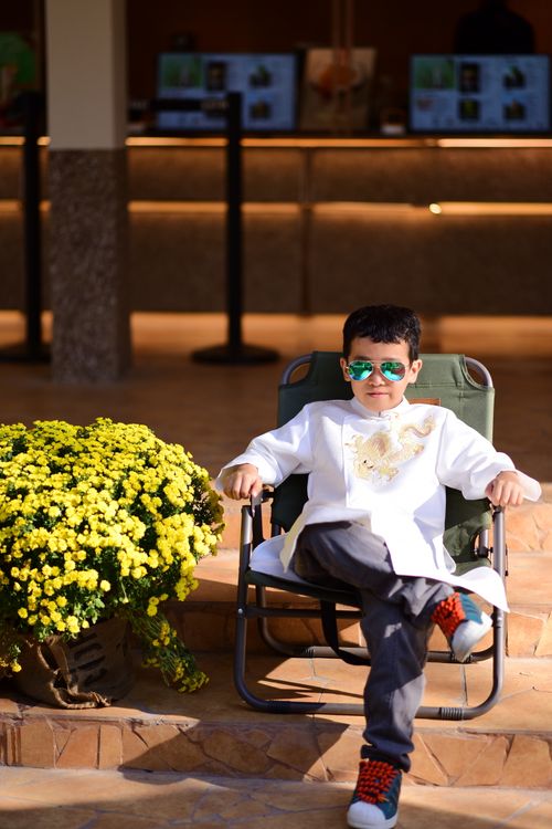 Free Stylish boy in sunglasses sits outdoors with yellow flowers in view. Stock Photo