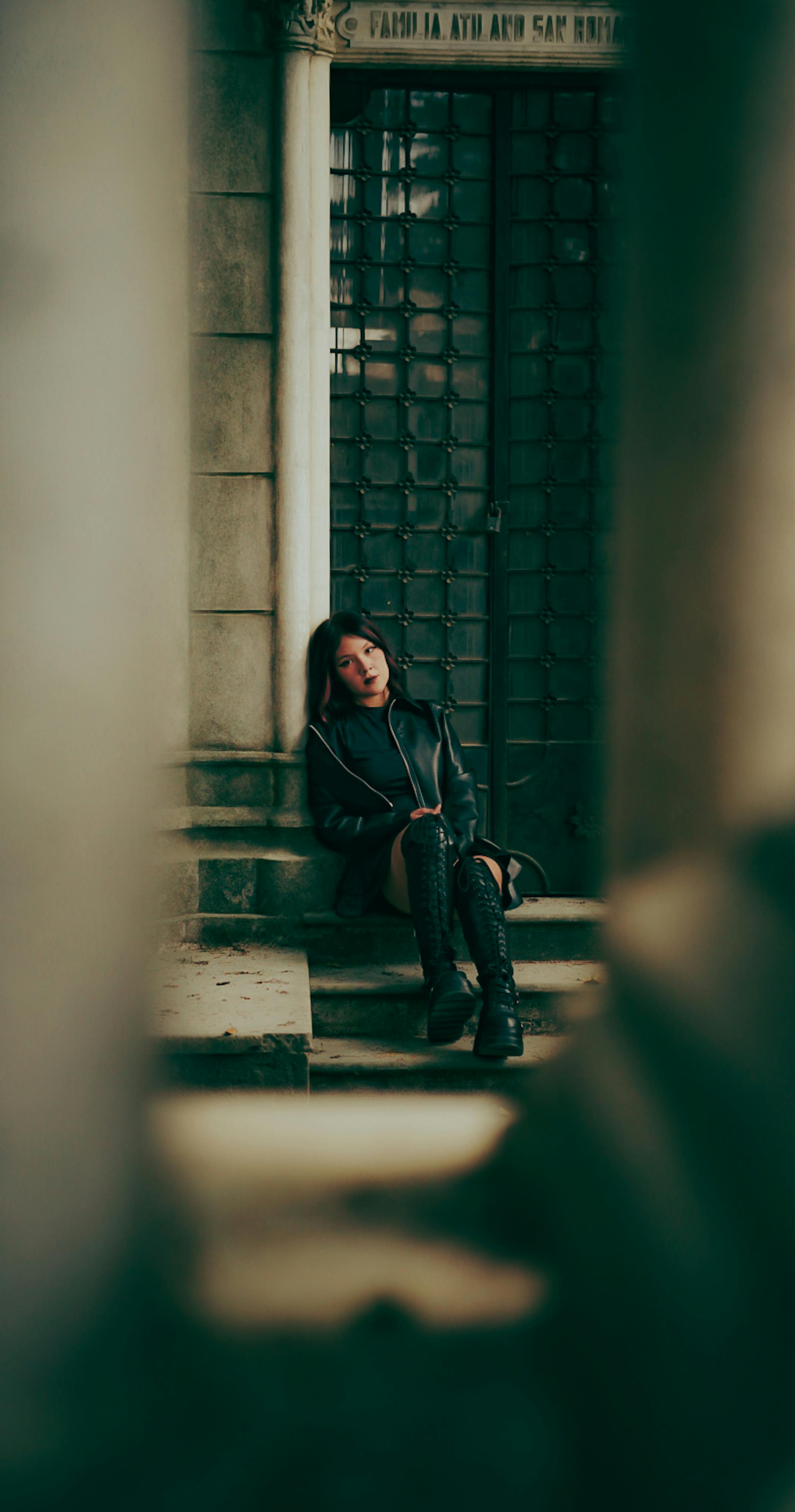 Free A thoughtful woman sits on stone steps in an urban setting, exuding a dramatic and moody tone. Stock Photo