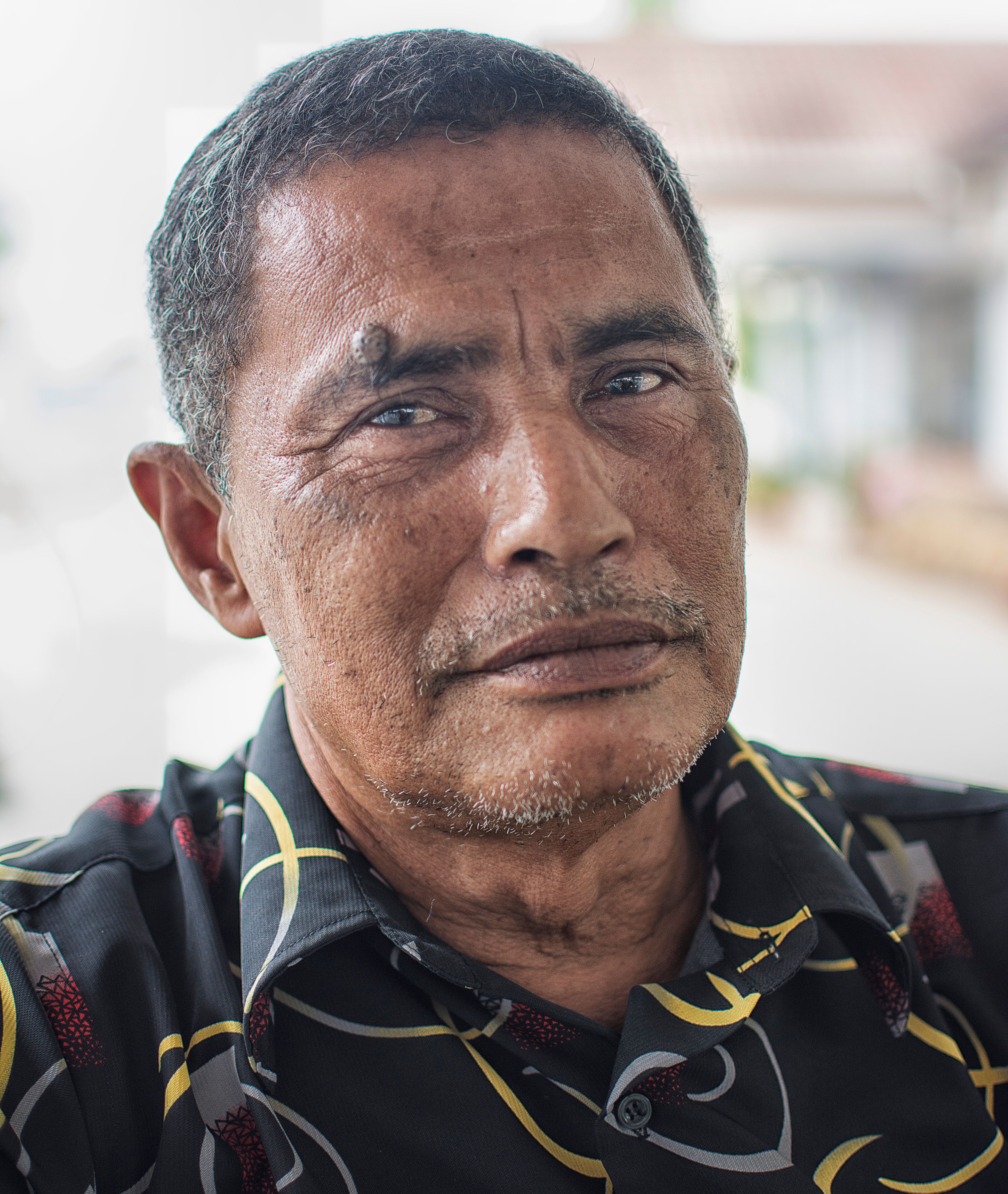 A thoughtful portrait of an adult man with a patterned shirt, captured indoors with a soft light.