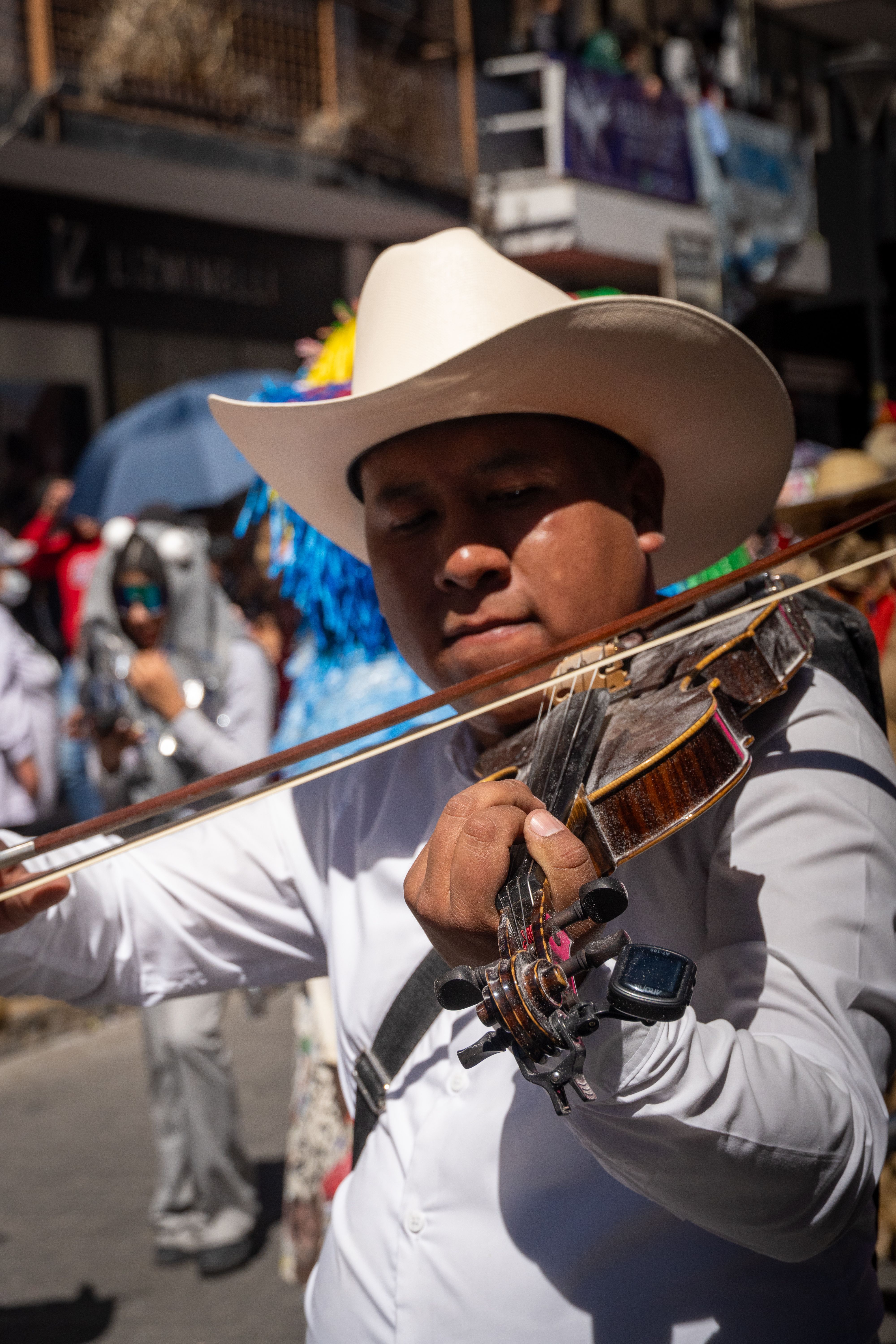 A musician in traditional attire plays the violin during a vibrant street carnival in Pachuca, Mexico.