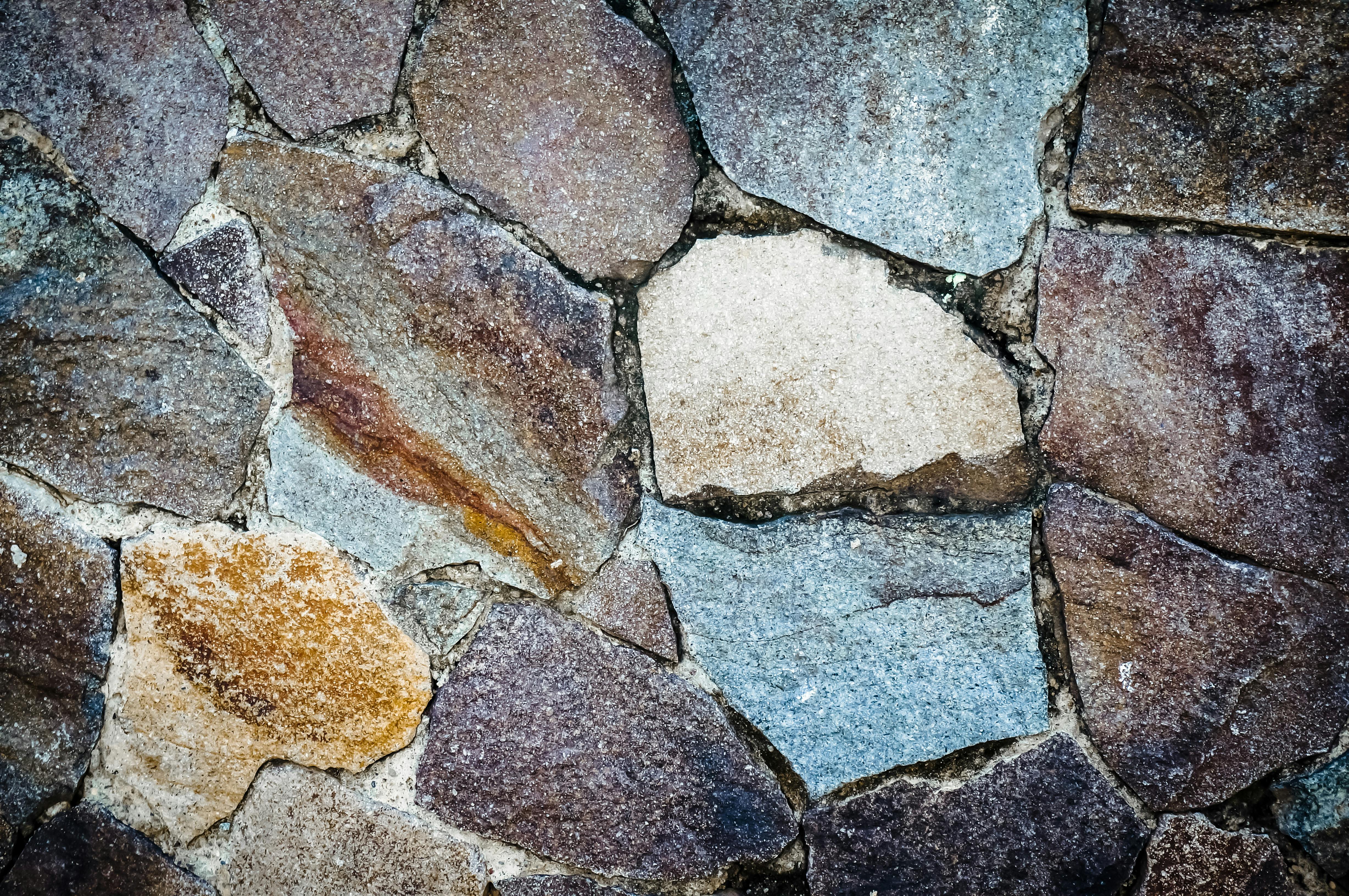 бесплатная Детальный вид красочной каменной стены, выполненной в различных формах и земляных тонах. Стоковое фото