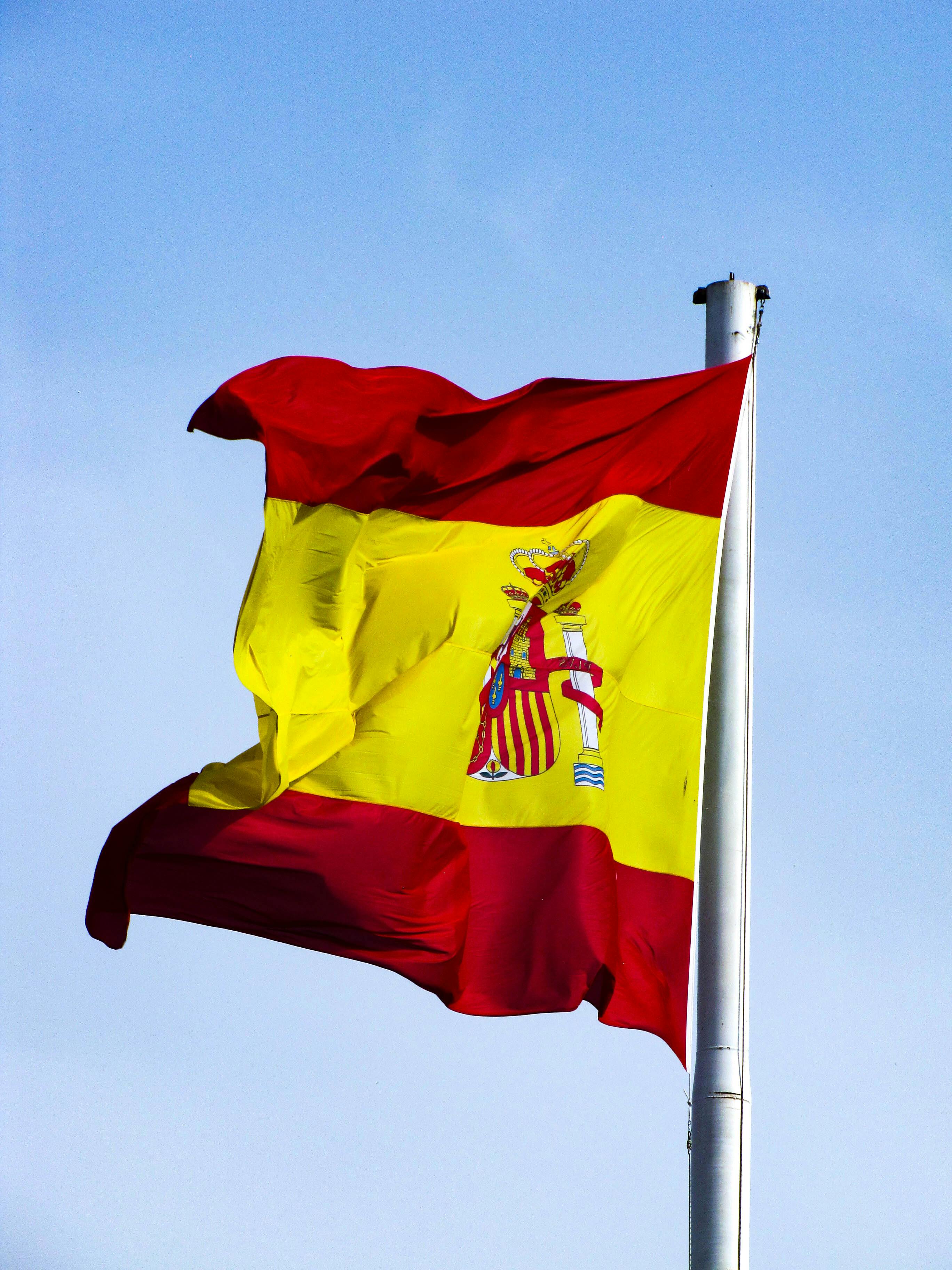 Gratis Det spanske nationalflag blafrer i vinden mod en klar blå himmel og viser national stolthed. Lagerfoto