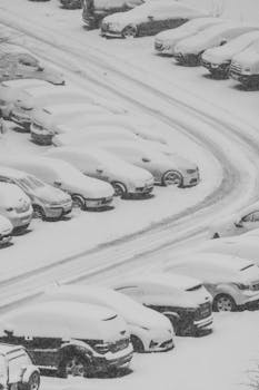 Aerial view of cars covered with snow in a parking lot during winter, showcasing a serene winter landscape.