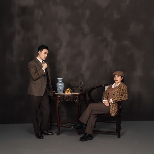Free A chic vintage-inspired portrait featuring two people in classic attire with vases on an ornate table. Stock Photo