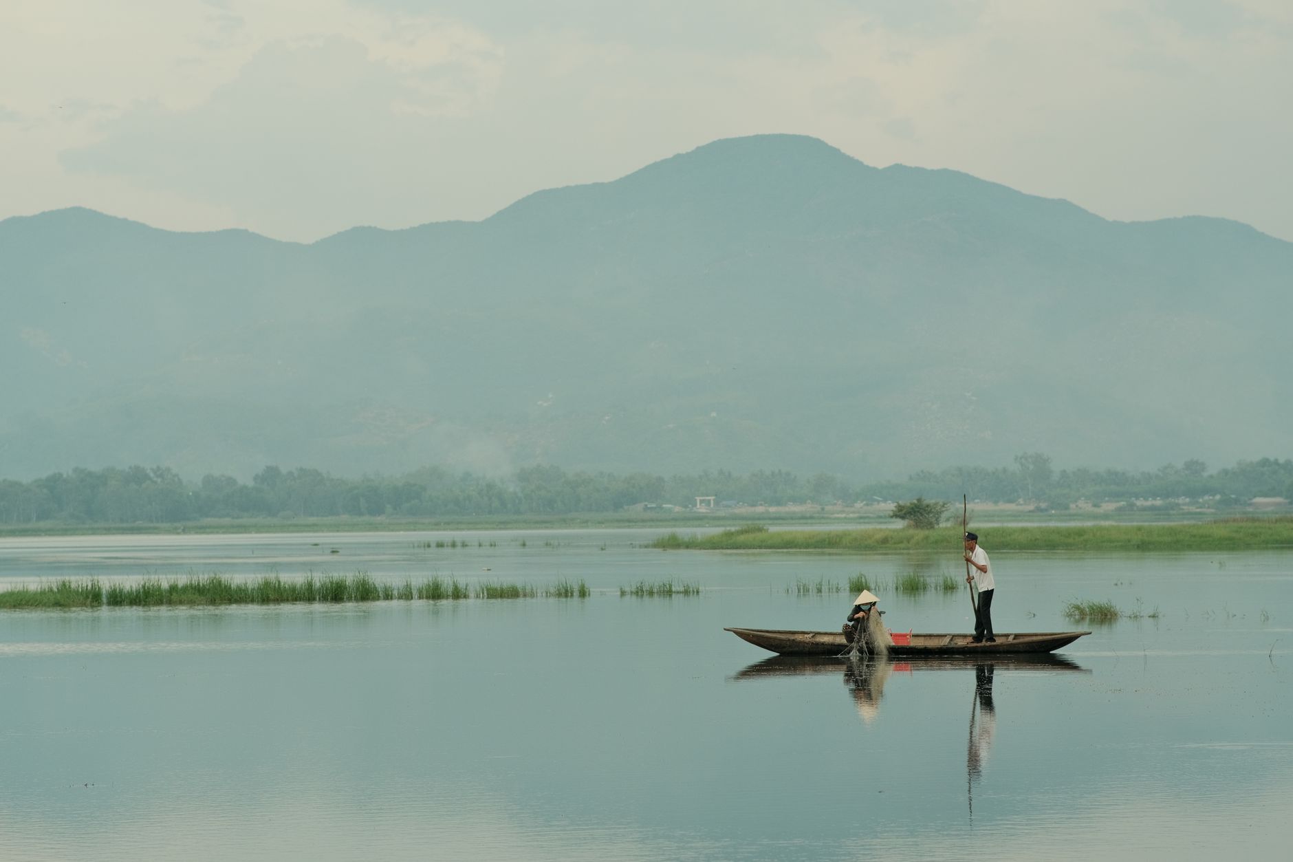 Serene view of a traditional fishing boat on a tranquil Vietnamese lake with mountain background.