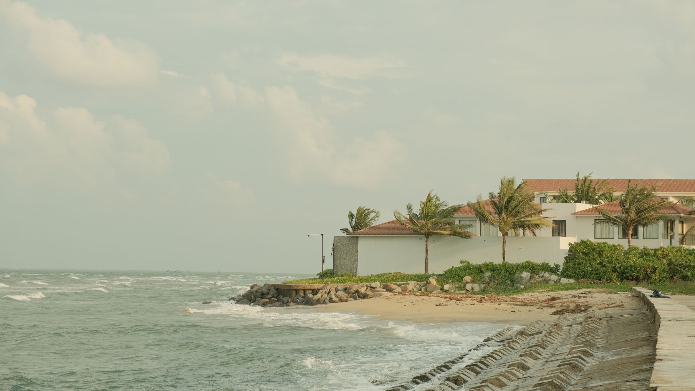 Peaceful view of a coastal resort in Hội An, Vietnam with gentle waves and palm trees.