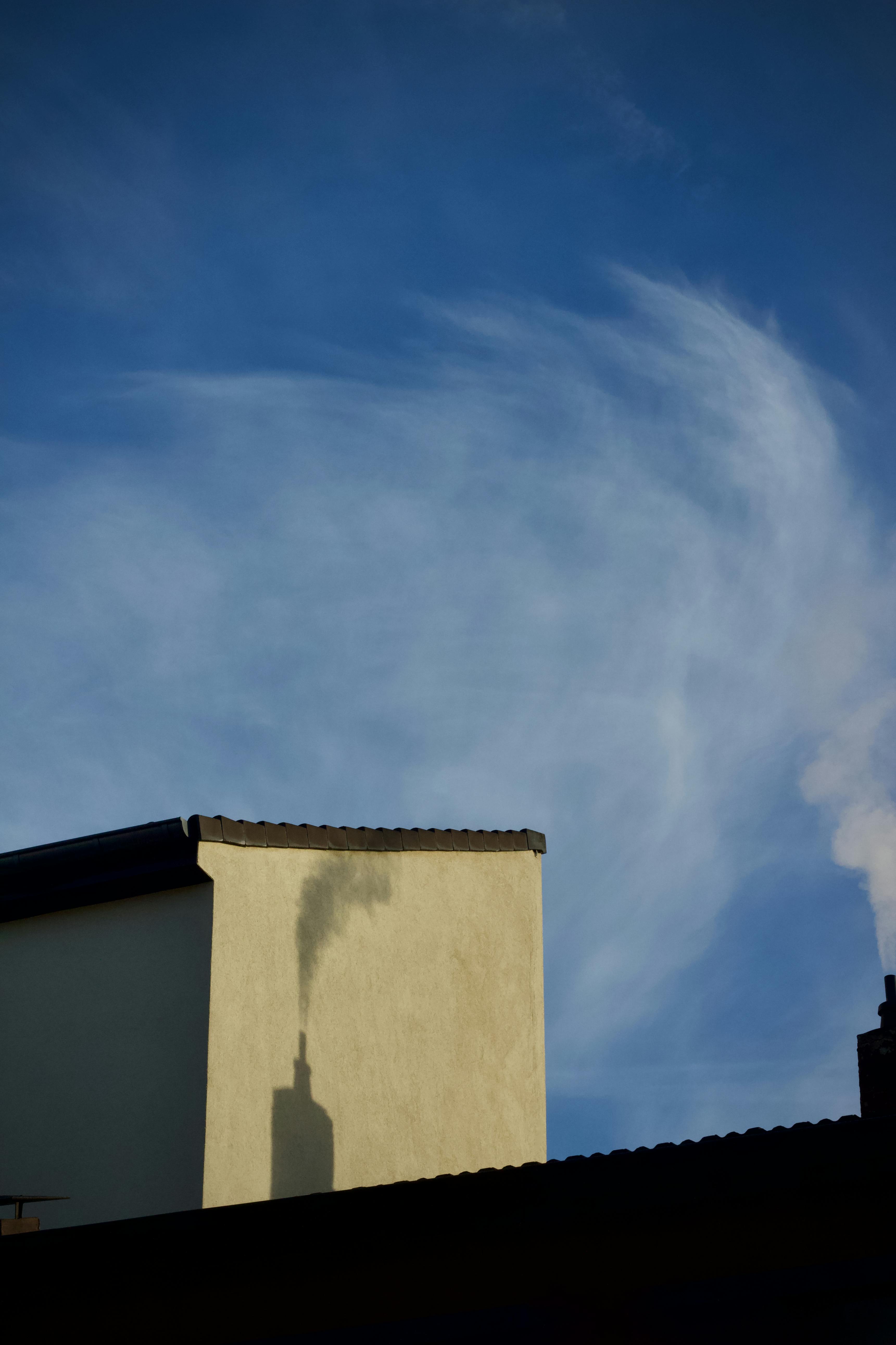 Gratis Skorsteinsrøyk kaster en skygge over bygningen med blå himmel i bakgrunnen, og fremhever bylivet. Arkivbilde
