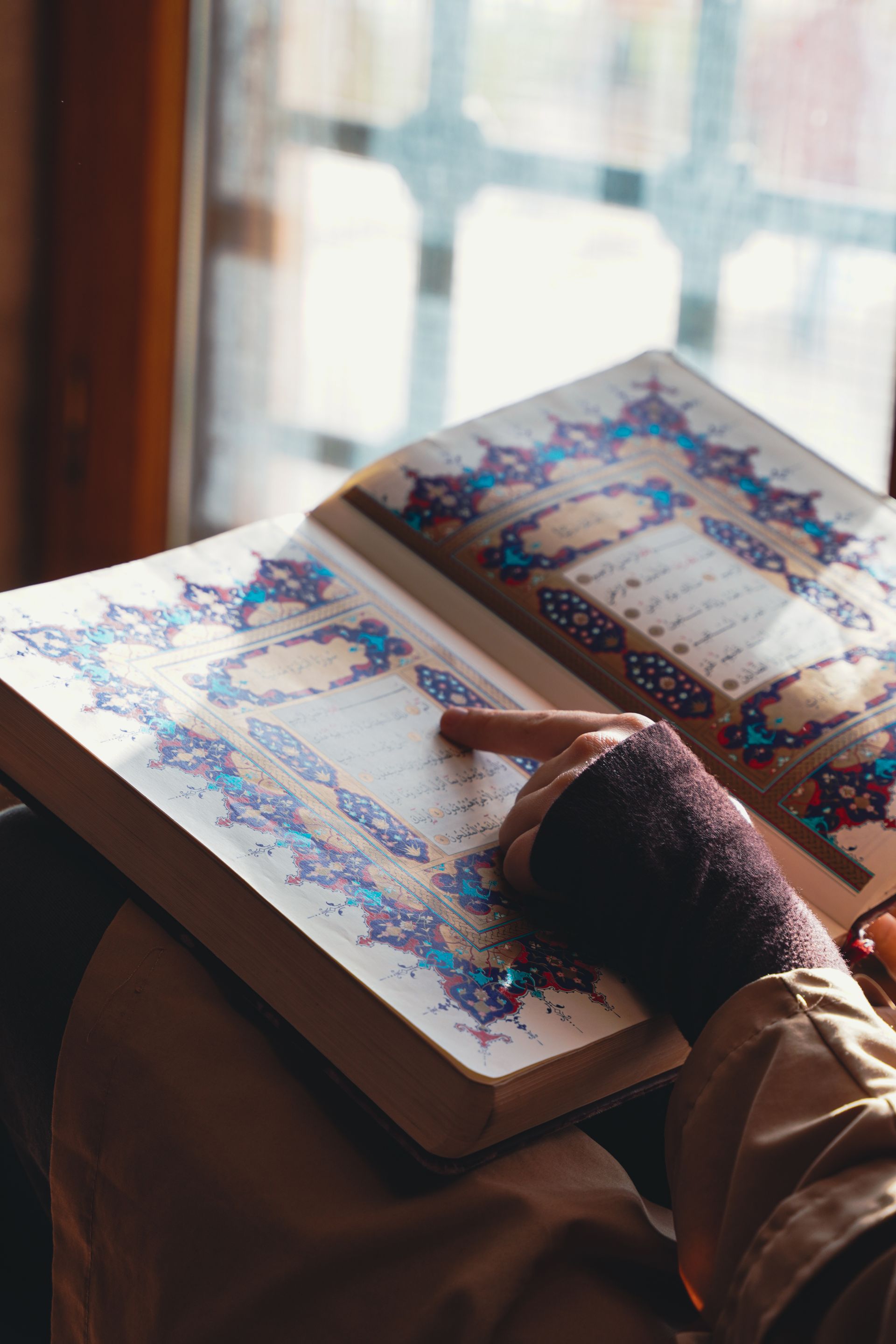 A person reading the Quran by a sunlit window