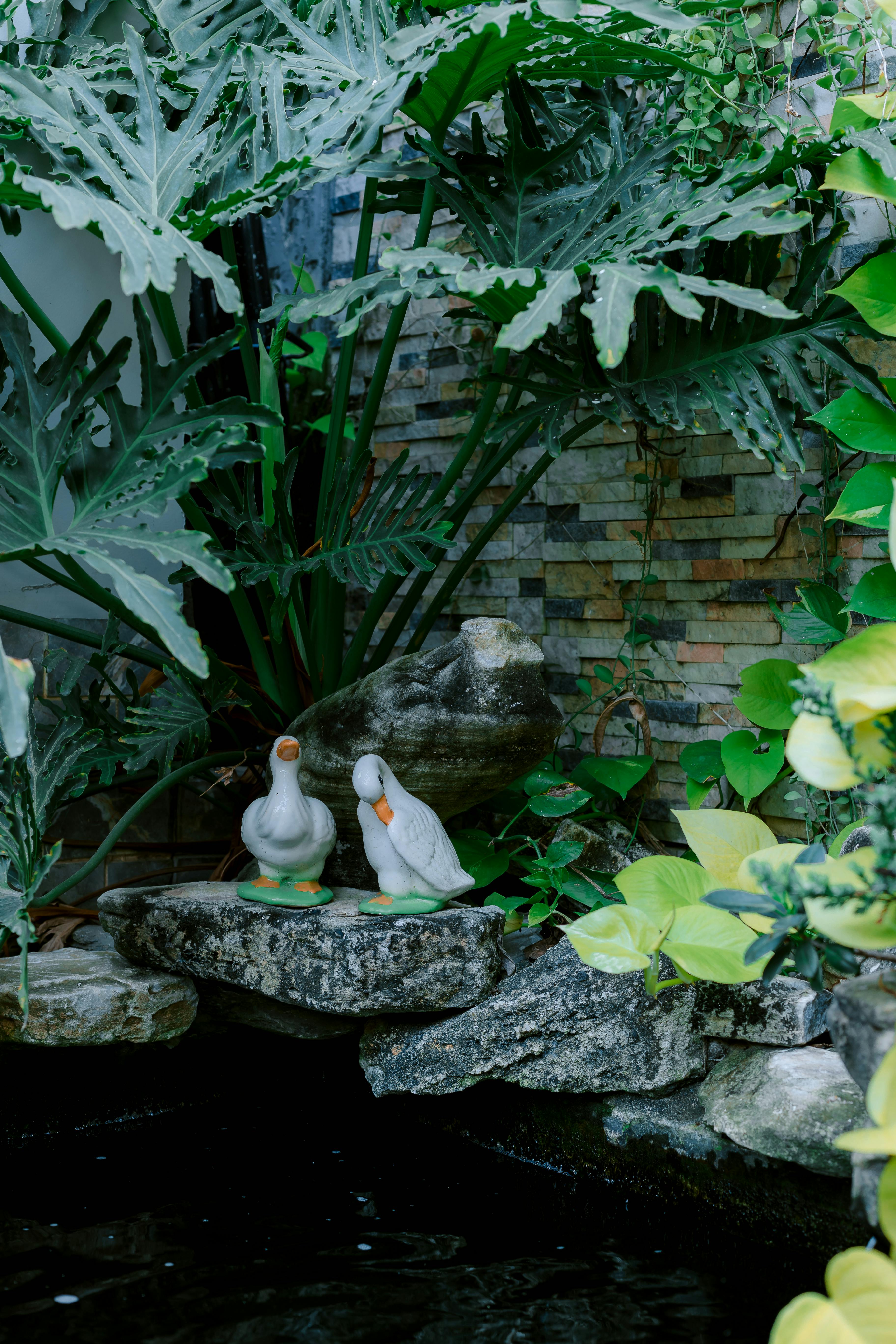 бесплатная Спокойная садовая картина с декоративными статуэтками уток и яркой зеленой листвой. Стоковое фото