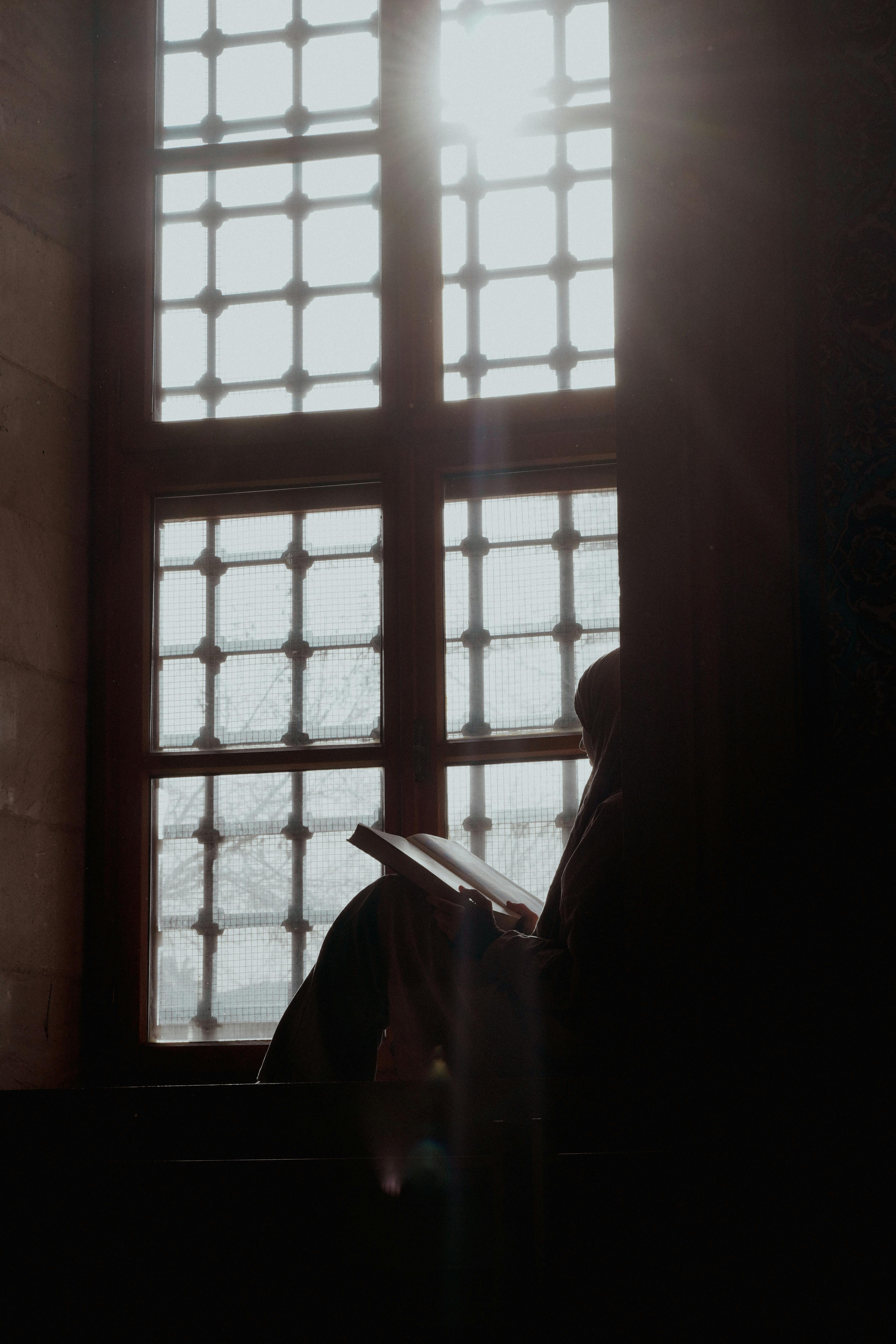 Free Silhouette reading by a lattice window with sunlight streaming in, Adana, Türkiye. Stock Photo