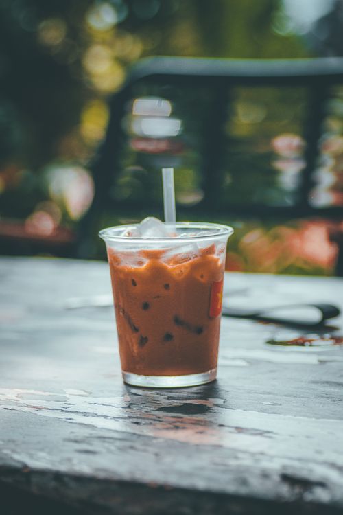 Free Chilled iced coffee in a clear cup placed on a wooden table, outdoors, with a blurred garden background. Stock Photo