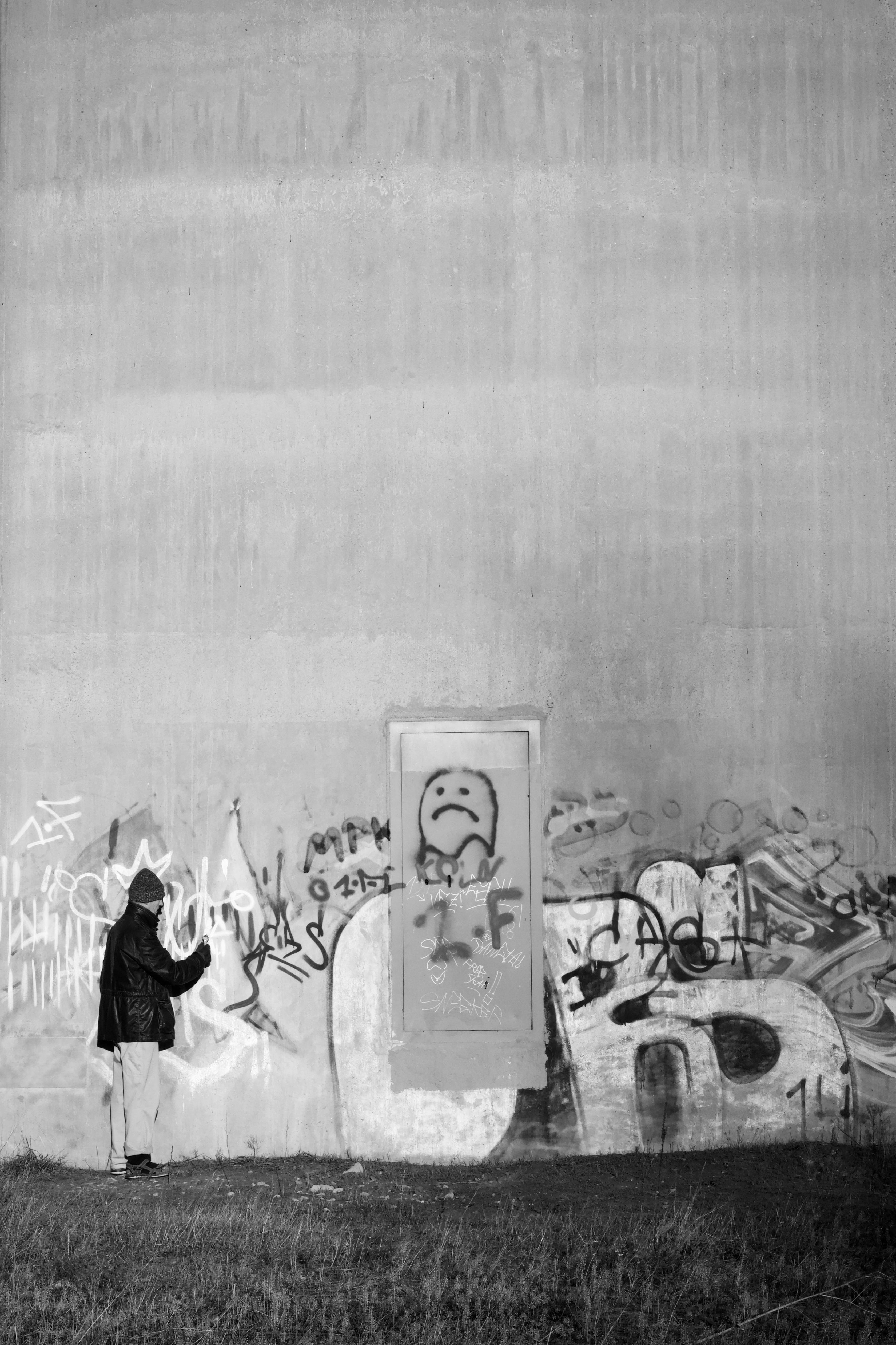 Ücretsiz Gece vakti, kapüşonlu bir figür büyük bir beton duvara sprey boyayla grafiti yapıyor ve kentsel sanat kültürünü sergiliyor. Stok Fotoğraflar