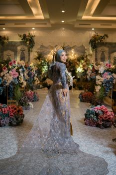 A bride in traditional Bugis attire poses amid vibrant floral arrangements during an Indonesian wedding ceremony.