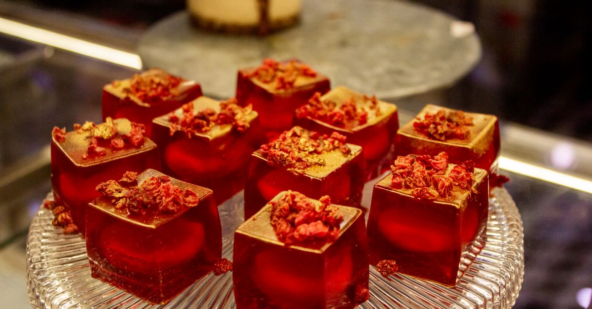 Elegantes doces de gelatina vermelha decorados com flocos de ouro e frutas vermelhas em uma travessa de vidro, perfeitos para apresentações gourmet.