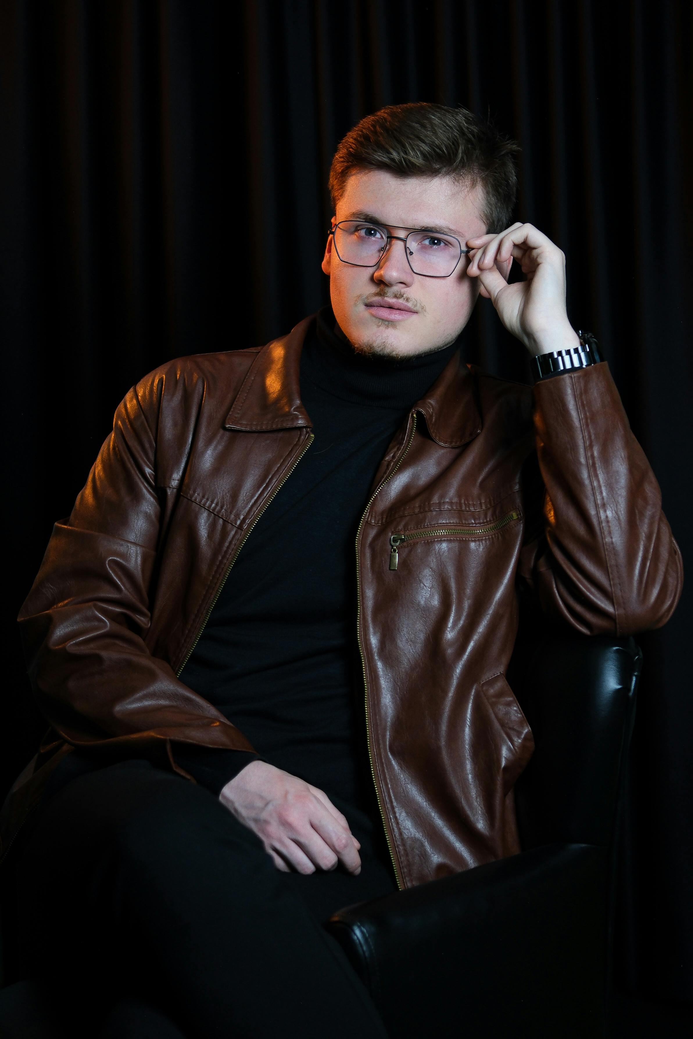 Gratis Mann sitter tankefull i en brun skinnjakke mot en mørk bakgrunn. Arkivbilde