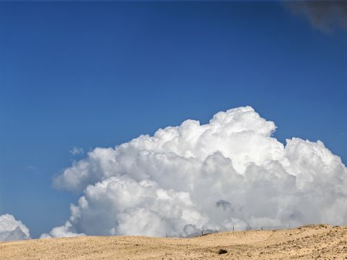 Free White fluffy clouds above a dry desert landscape under a clear blue sky. Stock Photo