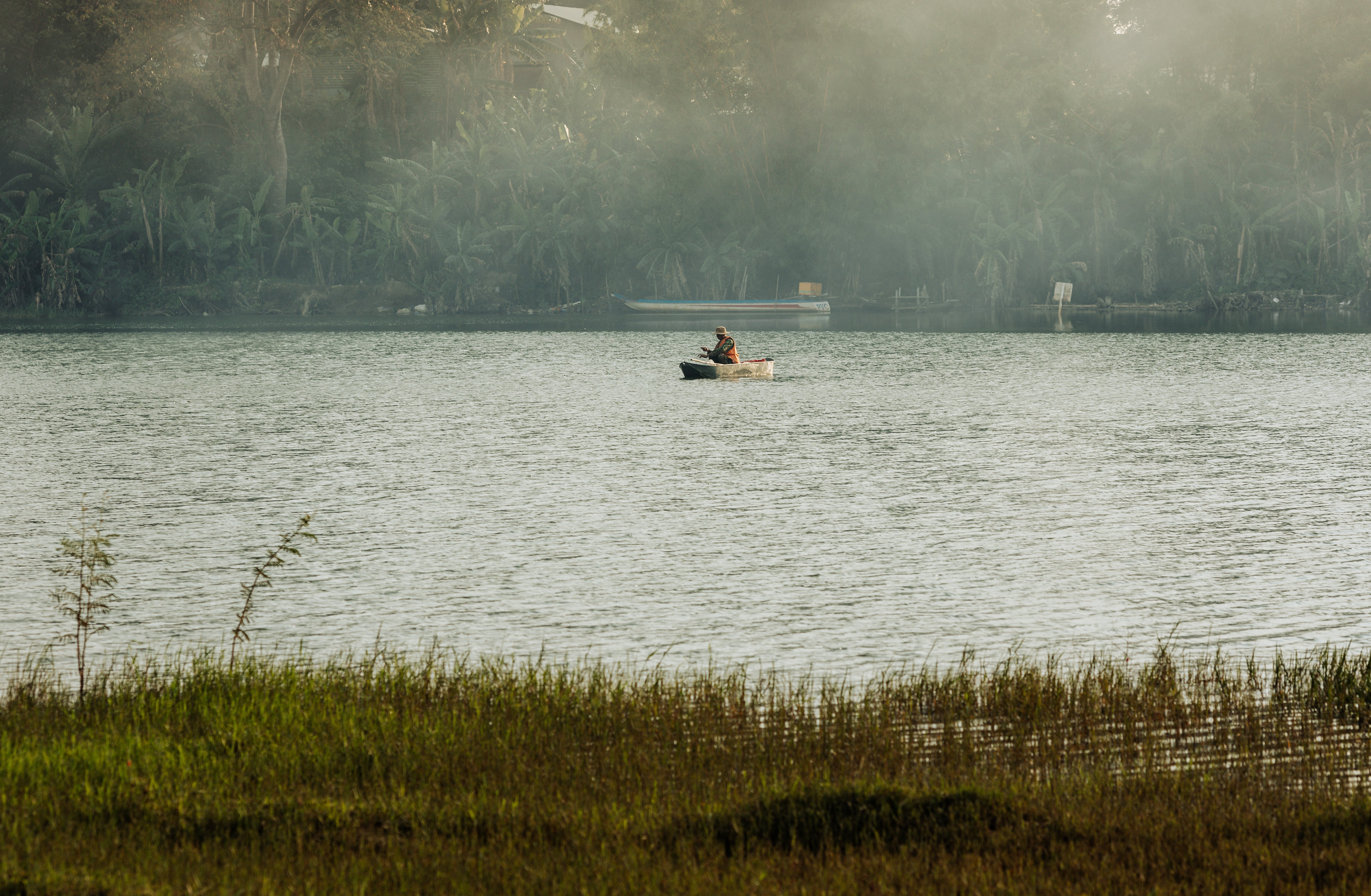 A lone fisherman in a small boat on a misty lake in Kon Tum, Vietnam.