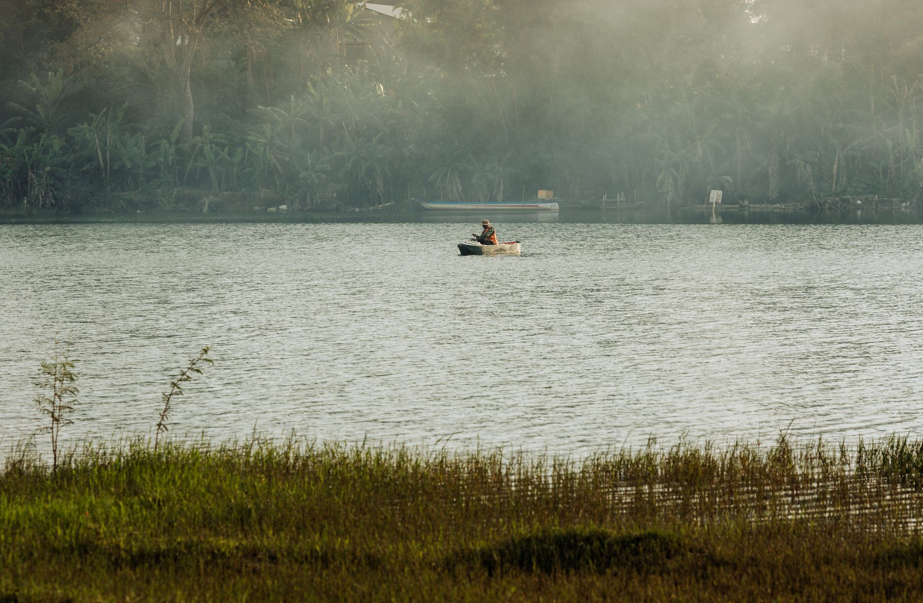 A lone fisherman in a small boat on a misty lake in Kon Tum, Vietnam.