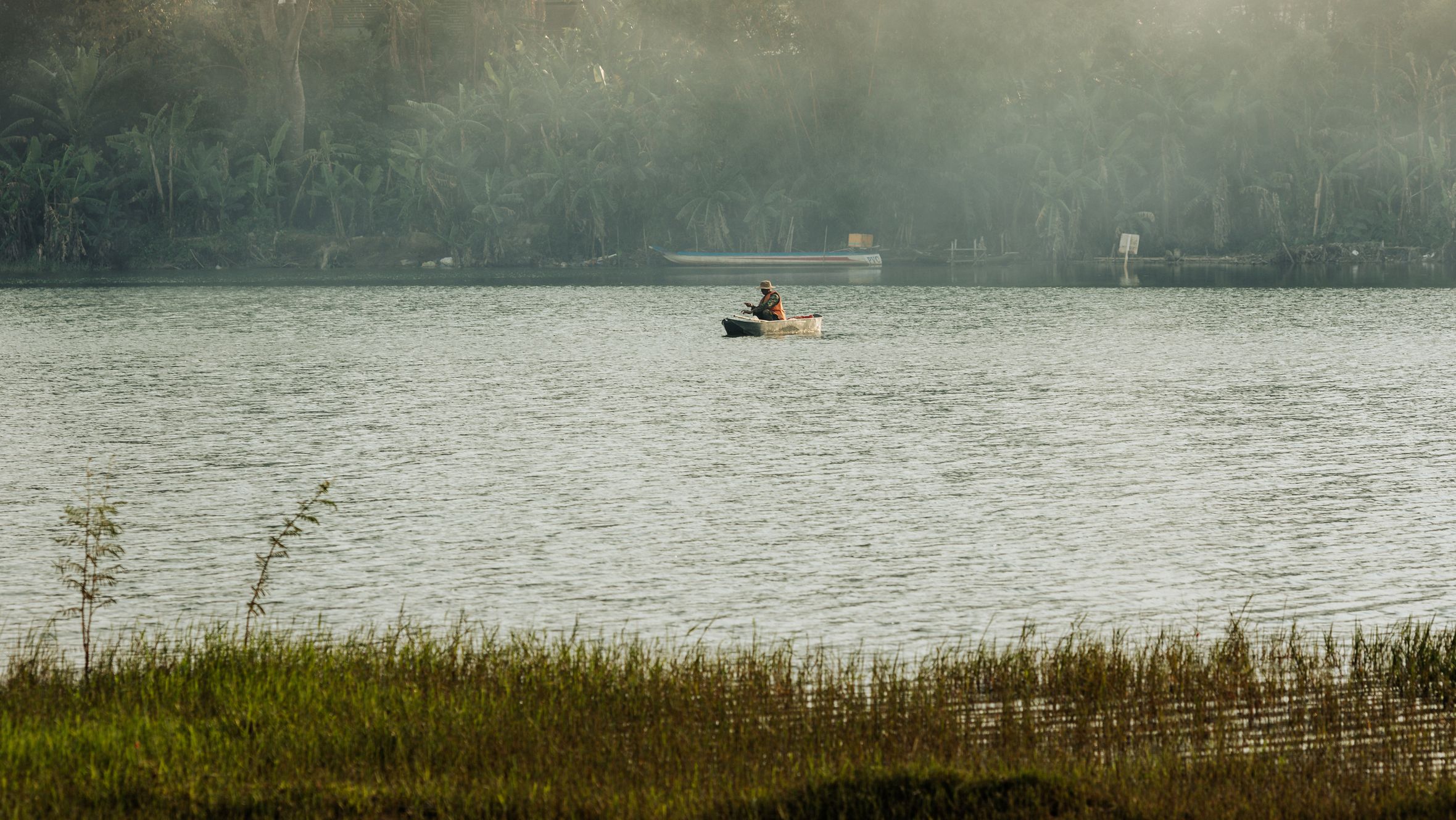 A lone fisherman in a small boat on a misty lake in Kon Tum, Vietnam.