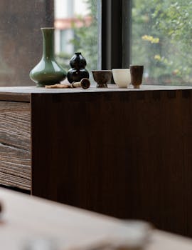A serene indoor still life featuring artful vases and tea cups on a wooden surface.