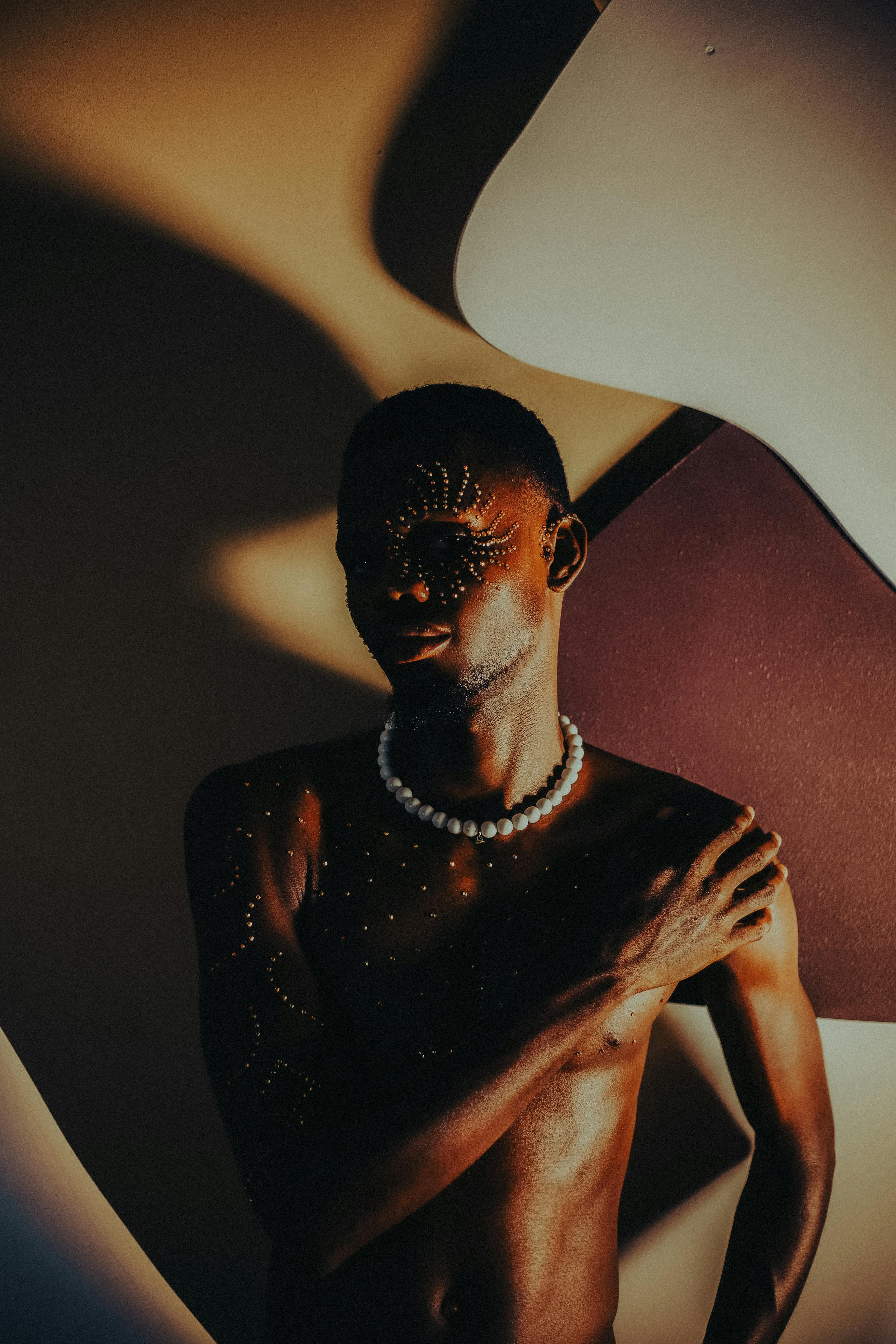 Free A dramatic artistic portrait of an adult man with painted tribal patterns and jewelry under creative lighting. Stock Photo