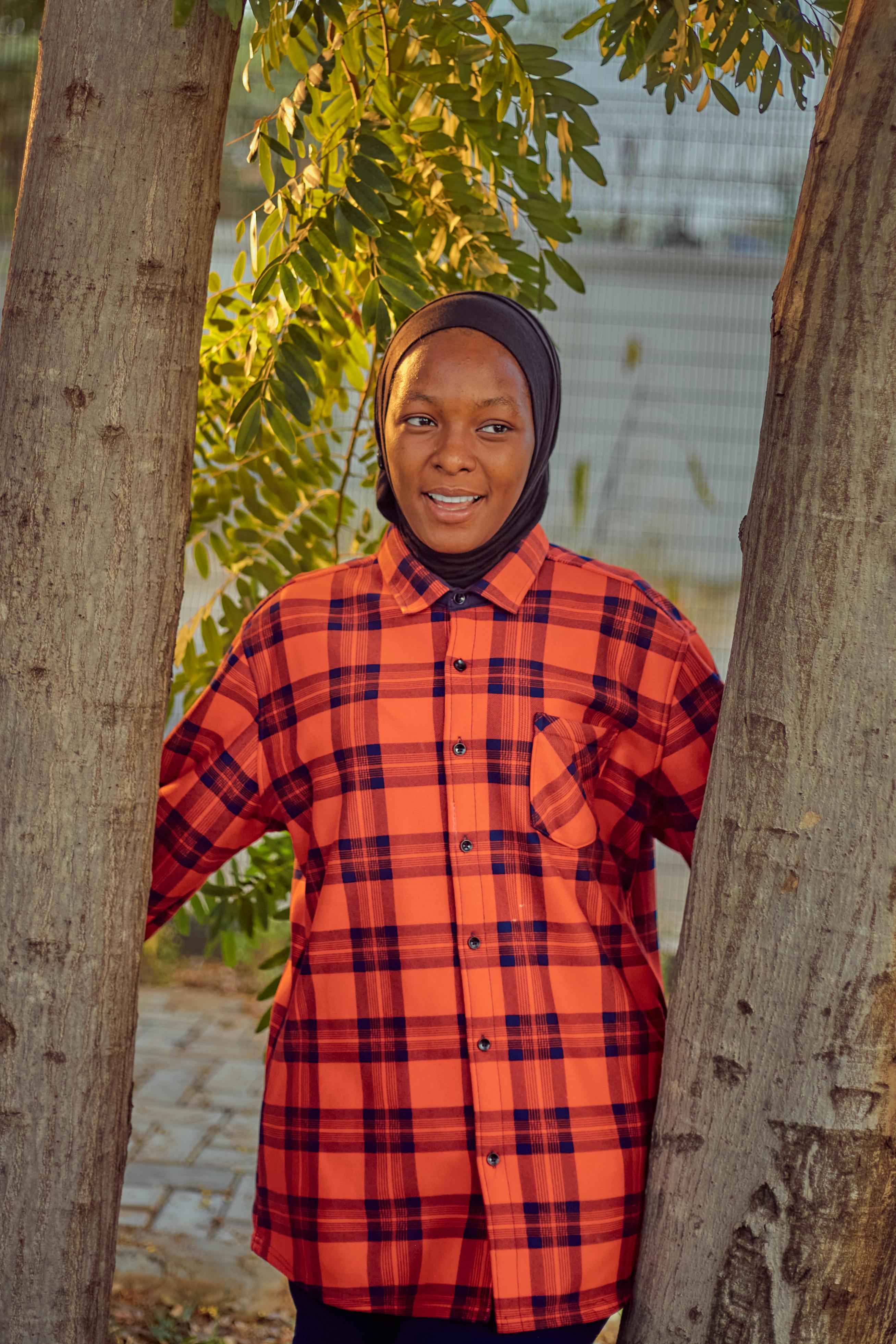 Gratis Smilende kvinde i ternet skjorte står udendørs mellem træer Lagerfoto