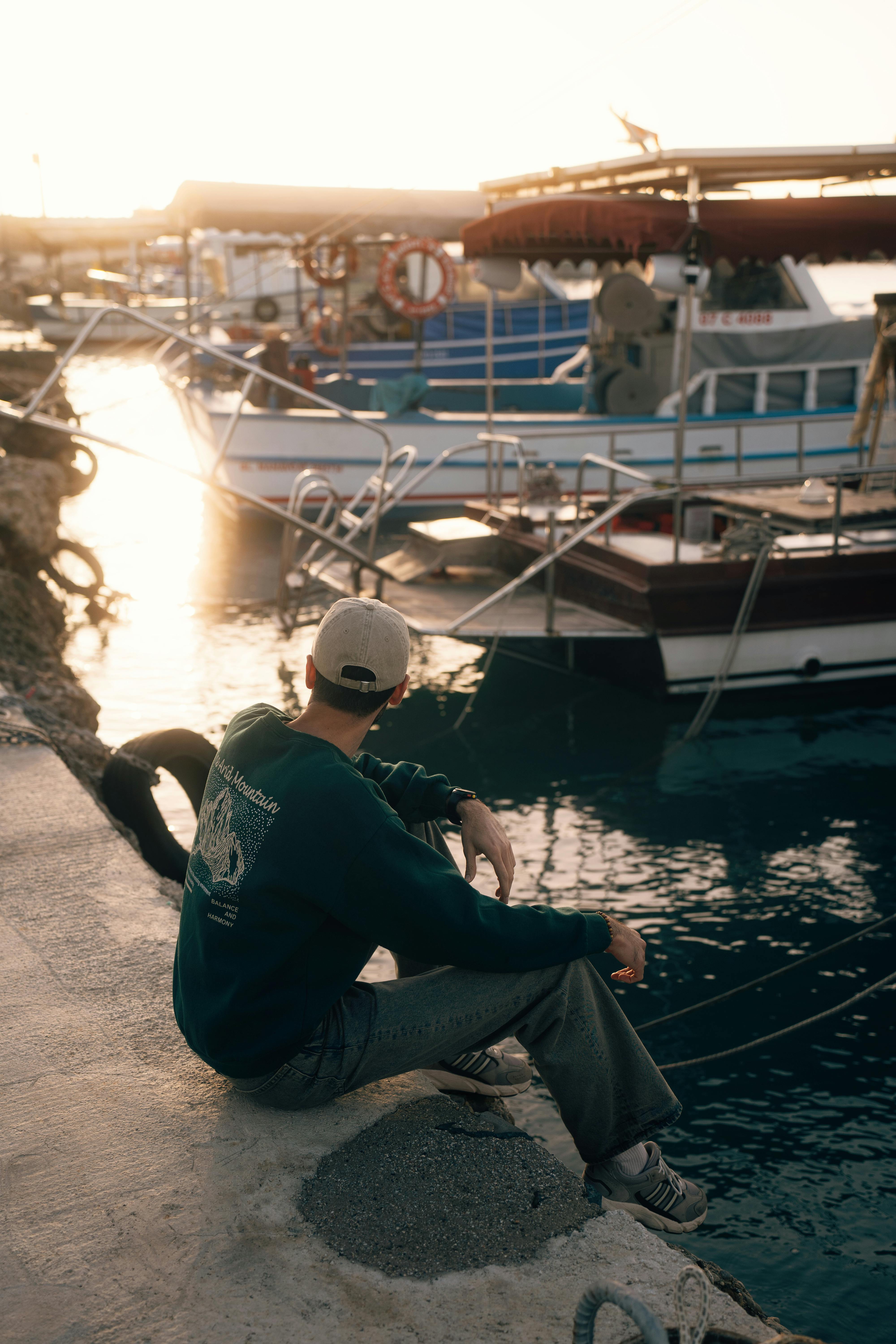 Gratis En ung mand sidder ved både i Antalya havn og nyder en fredfyldt solnedgang. Lagerfoto