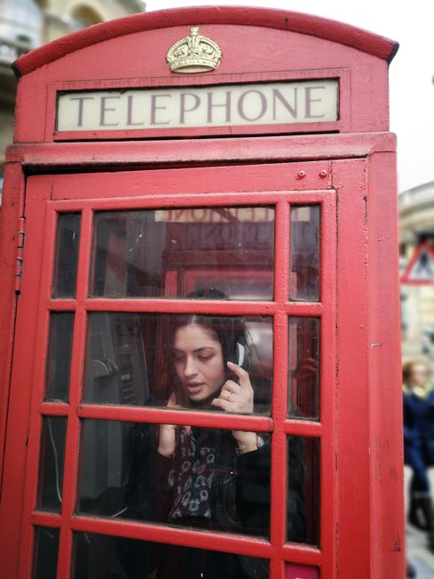 A woman using a vintage red telephone booth in London, capturing British nostalgia.