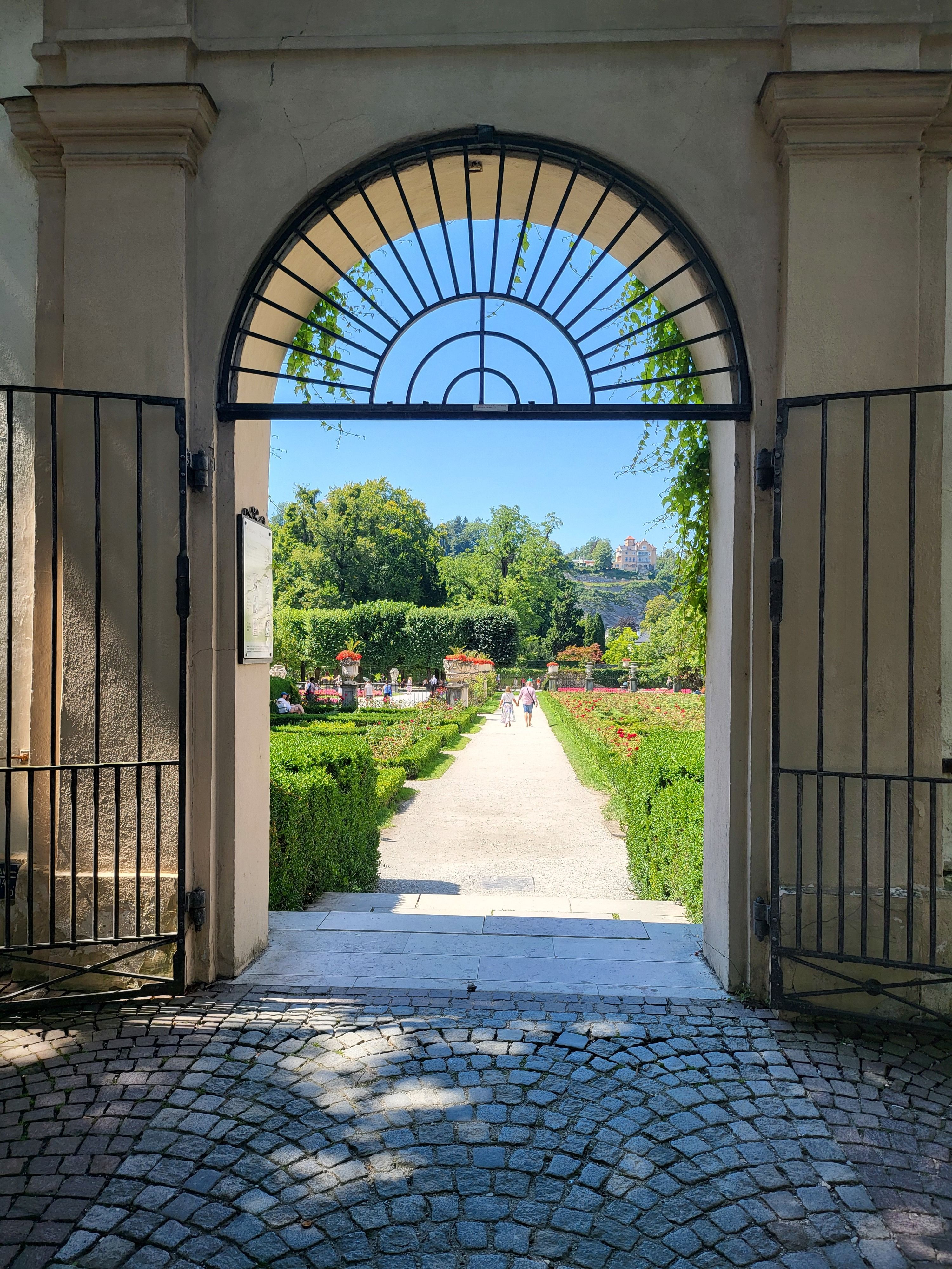 Charming view of Mirabell Gardens framed by an ornate archway, showcasing lush greenery.