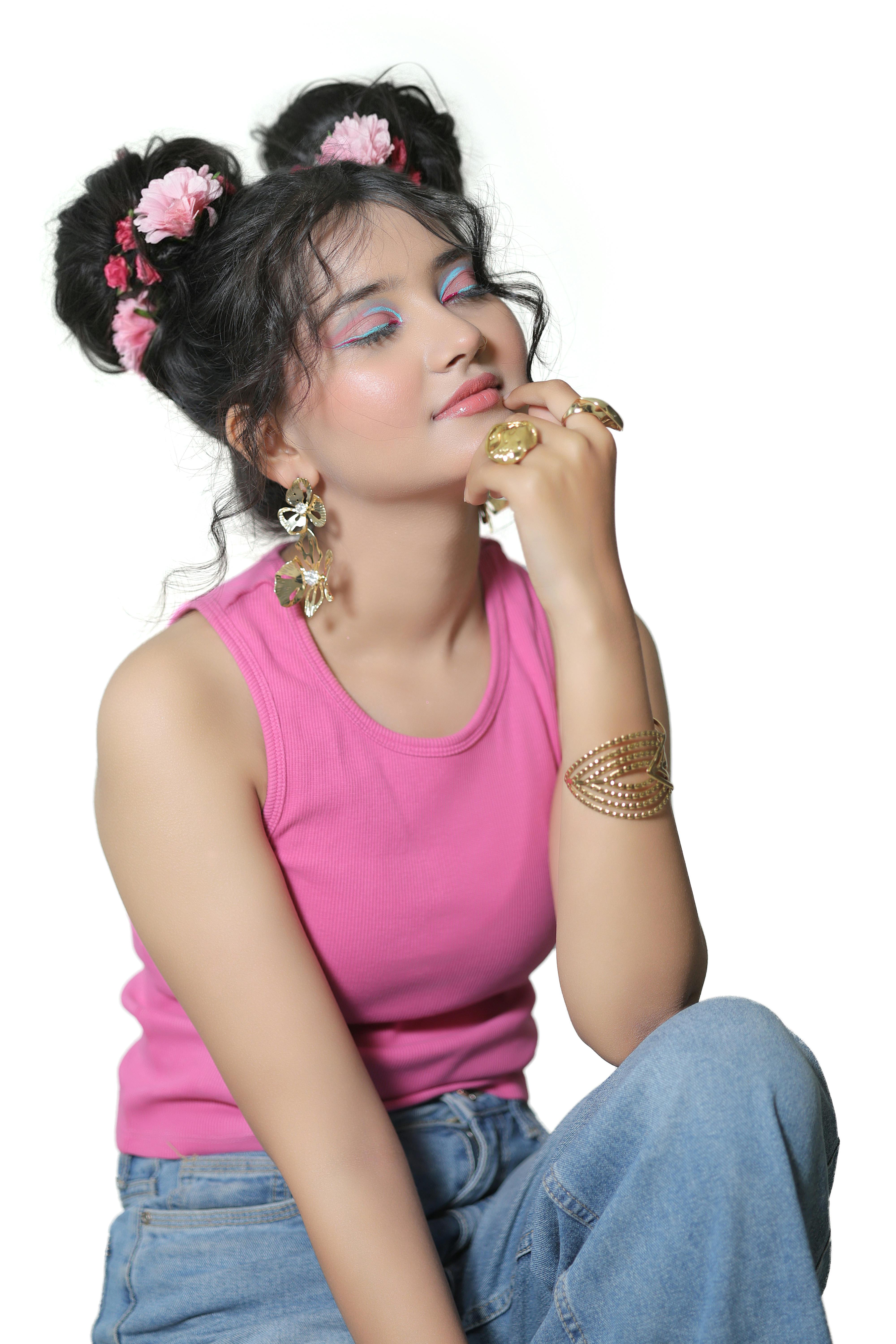 Gratis Una donna alla moda con chignon floreali, indossa un top rosa e jeans, il tutto completato da gioielli. Foto a disposizione