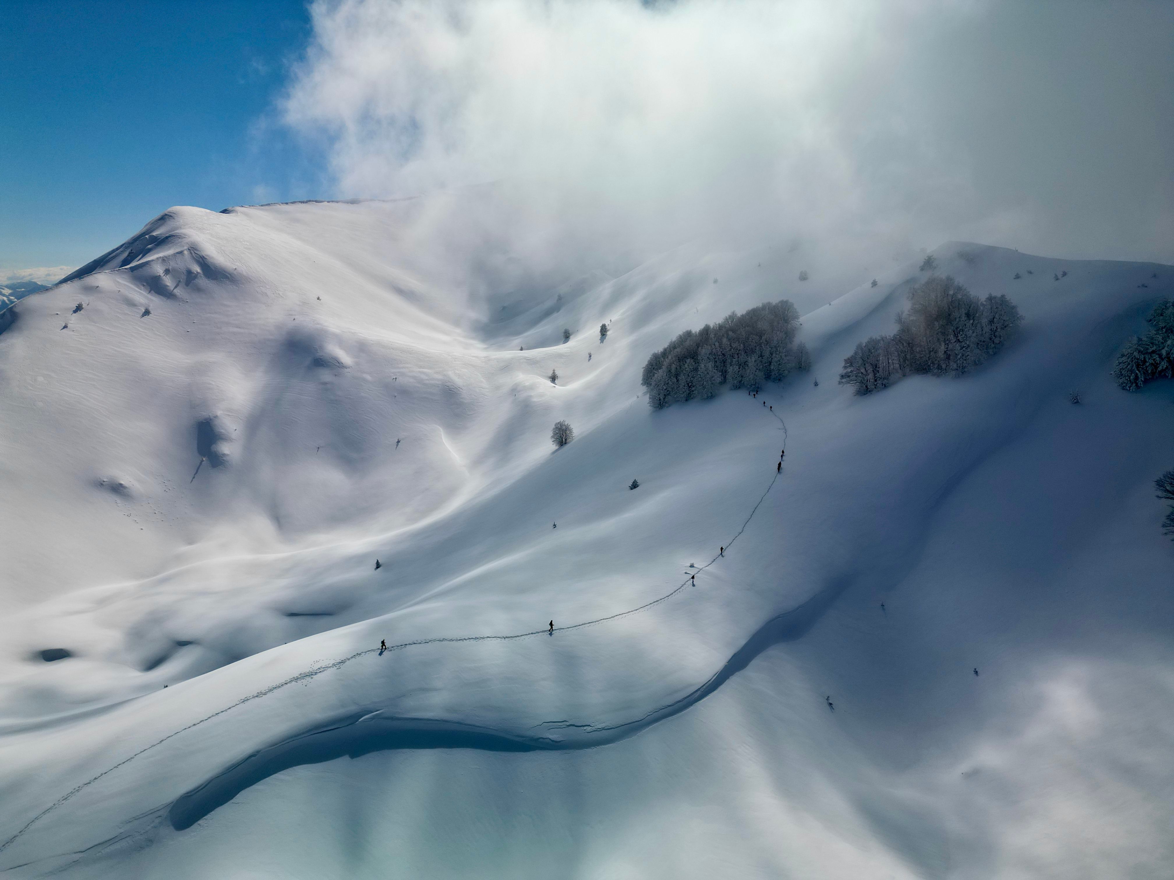 Aerial view of skiers climbing across snow-covered mountains under drifting cloud in Dibër County, eastern Albania