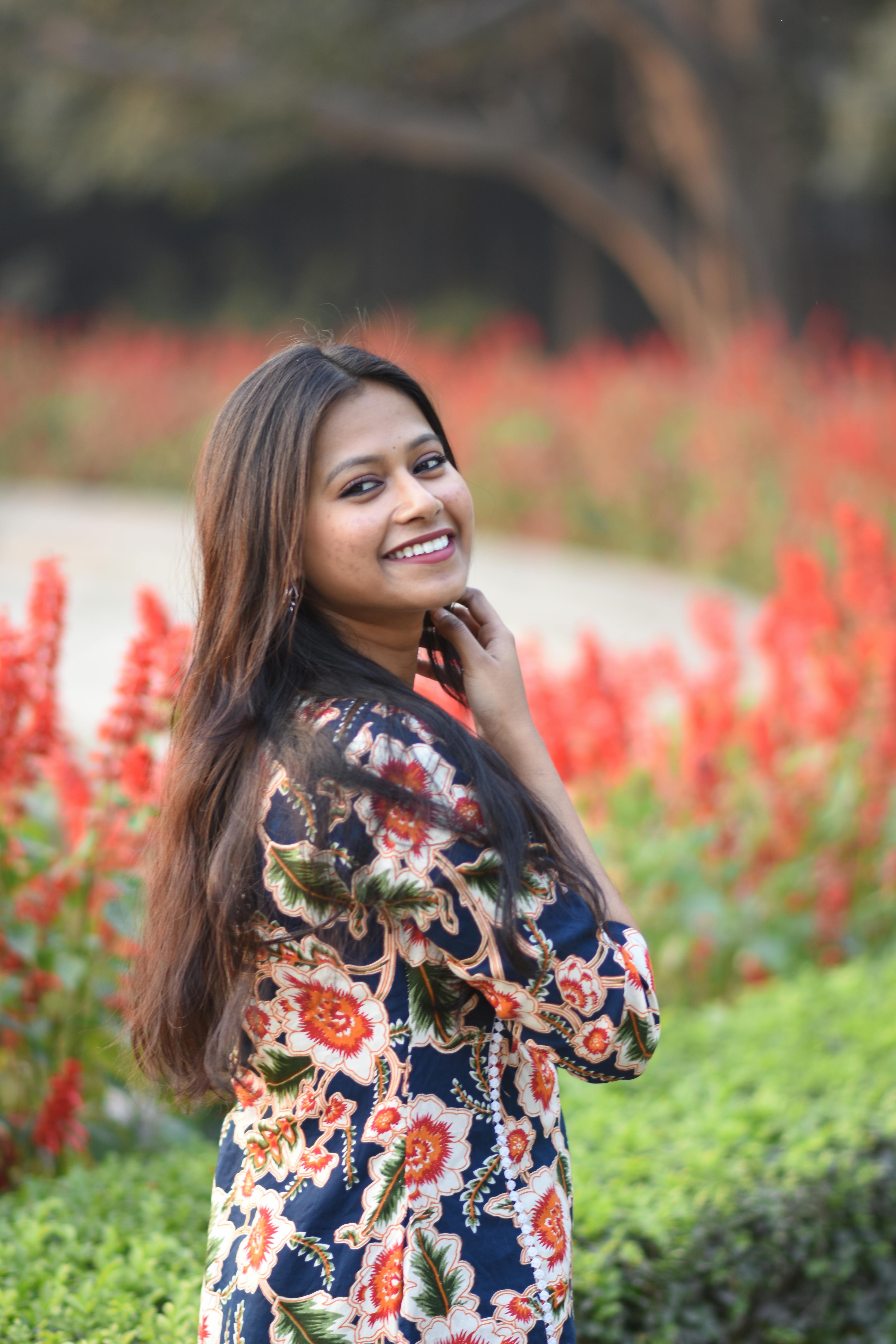 South Asian woman smiling in an outdoor garden with red flowers in Kolkata, India.