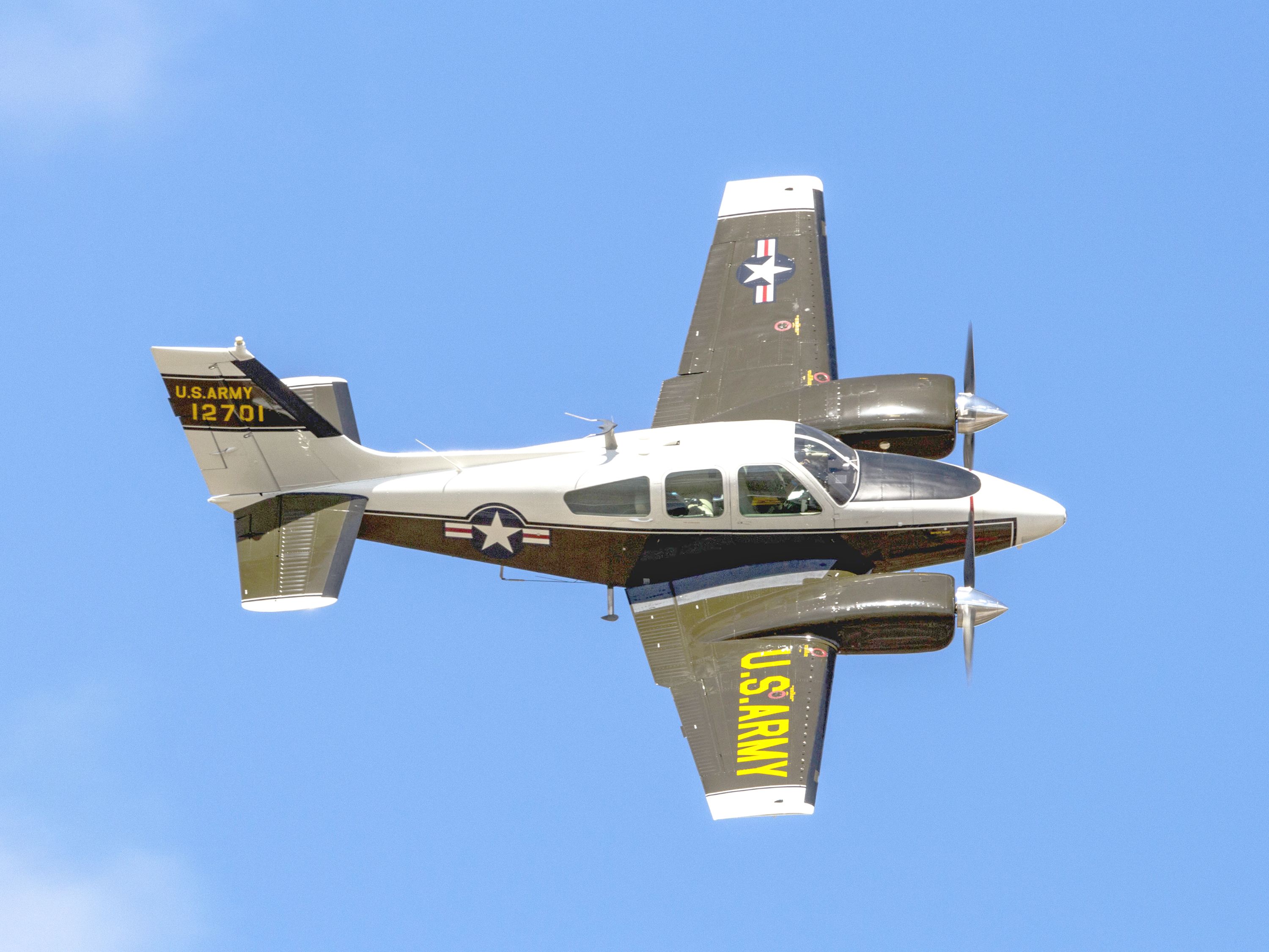 Beechcraft E55 Baron aircraft flying under clear blue skies during daytime.
