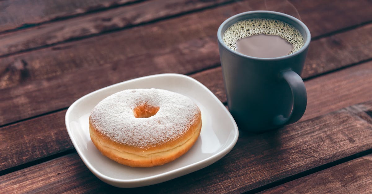 Doughnut On White Ceramic Plate Beside Ceramic Mug On Brown Wooden Table