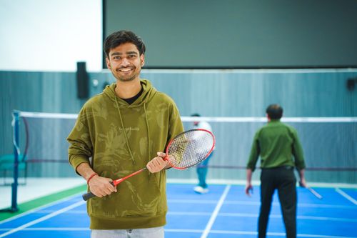 Free Portrait of a young man holding a badminton racket indoors, ready to play. Stock Photo