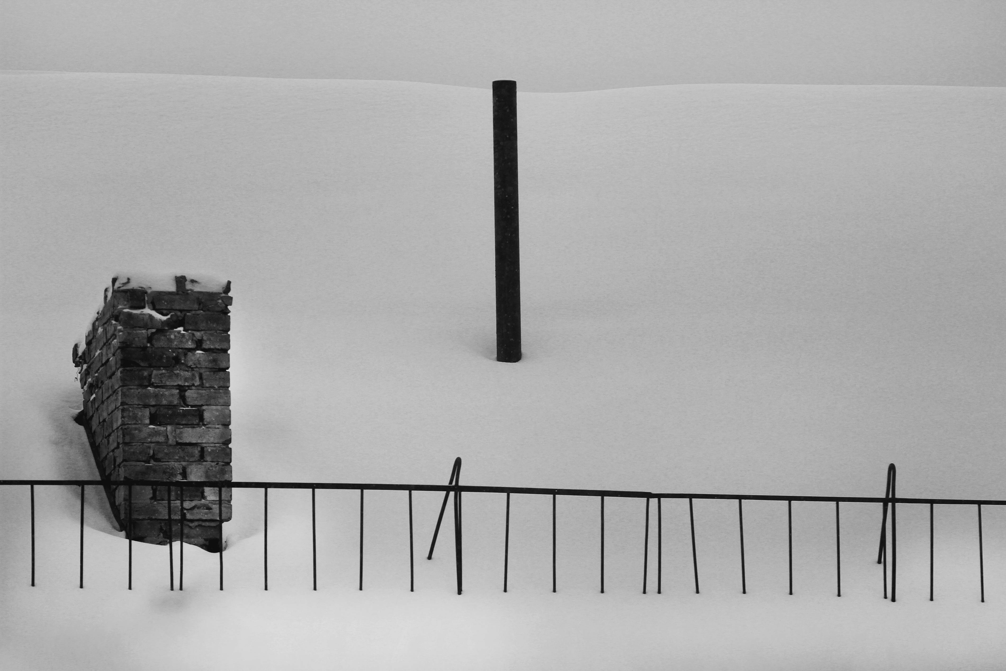 bezplatná Černobílá fotografie cihlové zdi a plotu v zasněžené krajině. Minimalistická a abstraktní kompozice. Základová fotografie