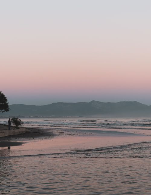 Free Peaceful beach scene at twilight with soft pastel hues and distant mountains, perfect for tranquil themes. Stock Photo