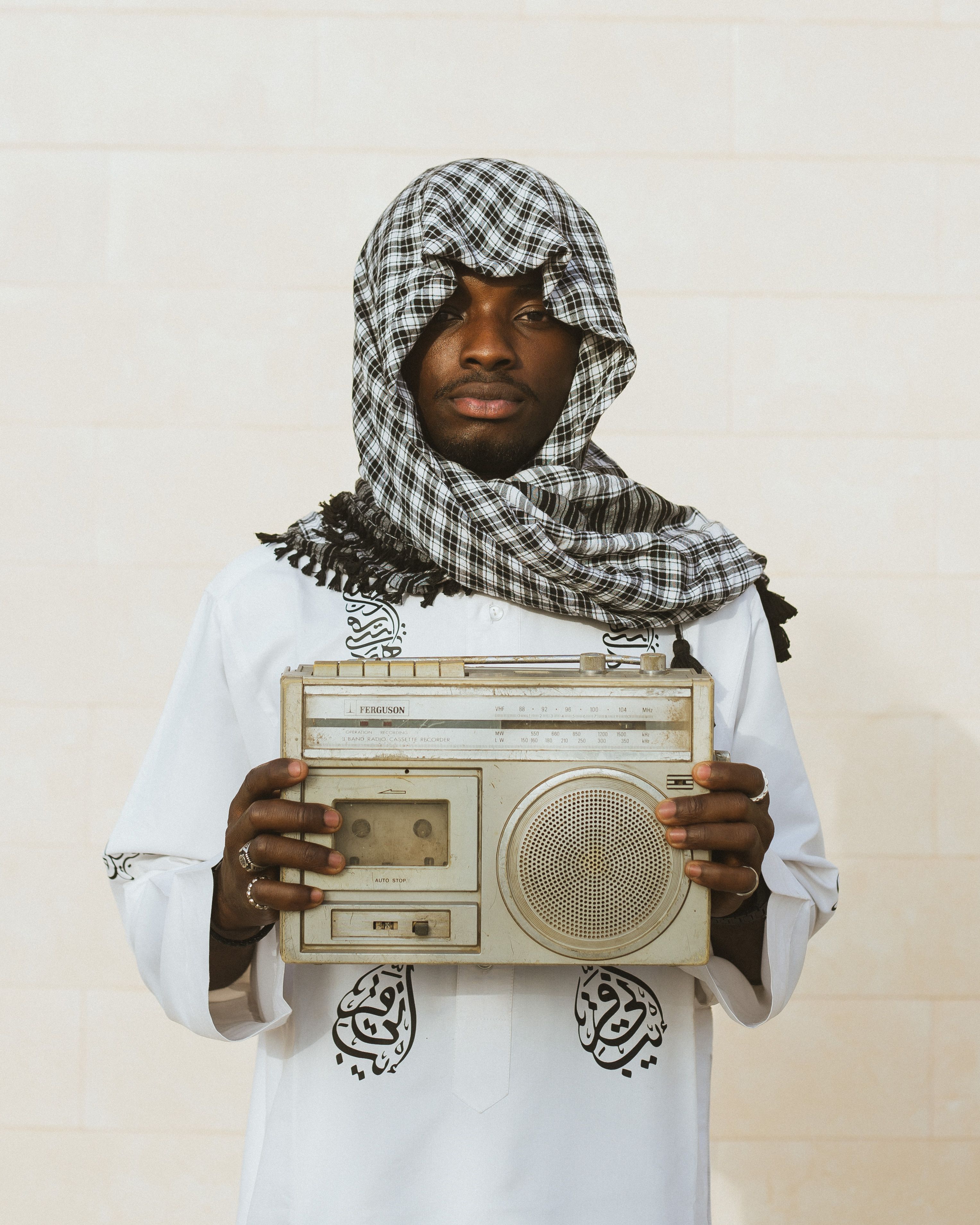 Portrait of an African man holding a vintage radio, wearing traditional garment and headscarf.