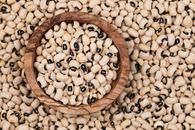 Overhead view of black-eyed peas in a rustic wooden bowl and scattered around, emphasizing a natural food theme.