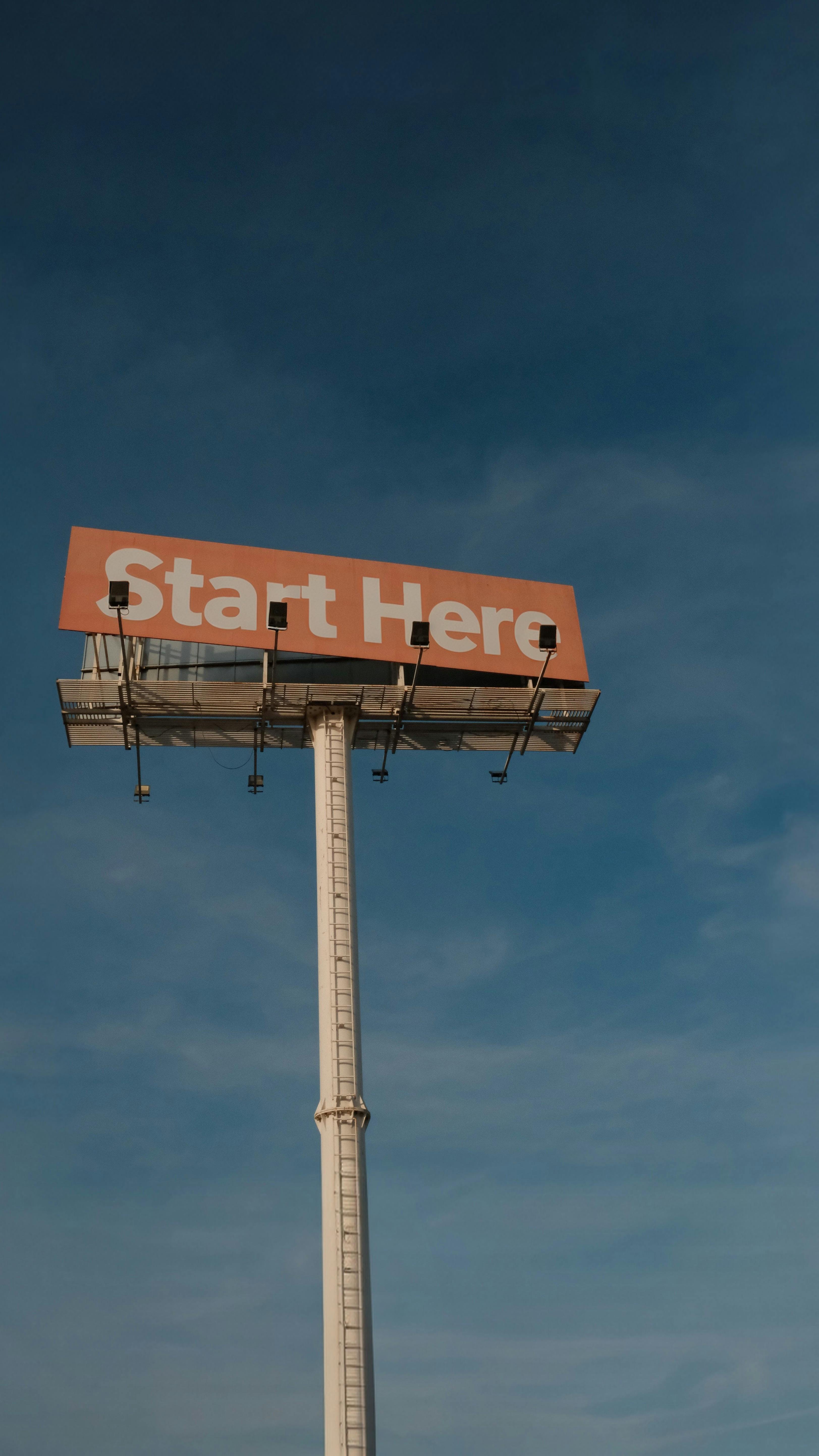 Free A tall billboard with 'Start Here' message set against a clear blue sky. Stock Photo