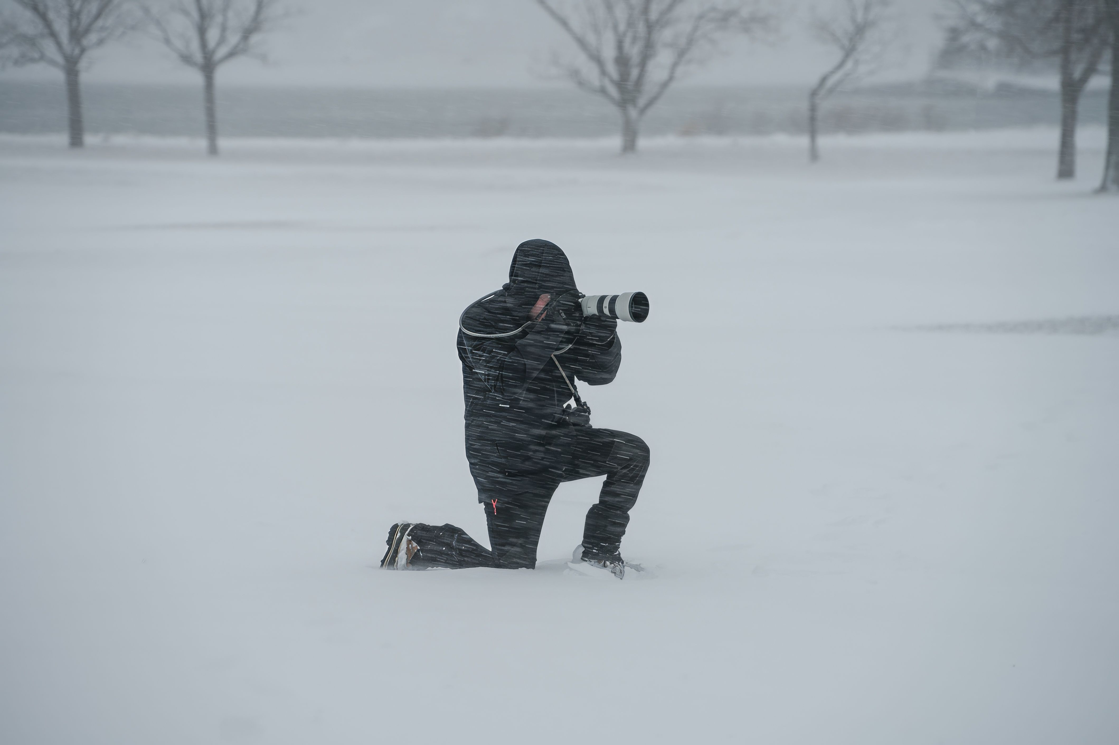 A dedicated photographer kneels in a snowy field, braving a winter storm to capture stunning images.