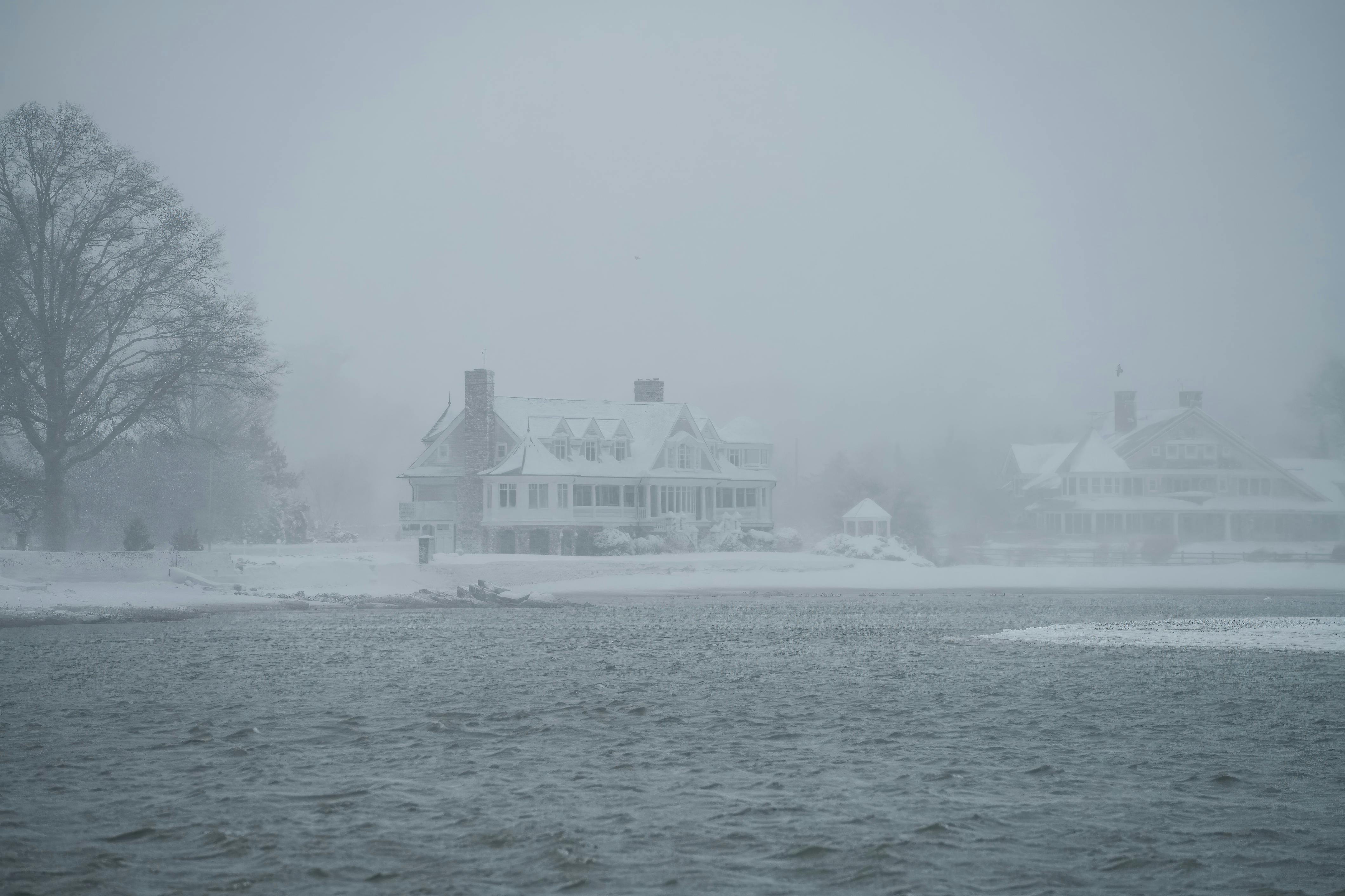 Gratis Rumah-rumah elegan di tepi danau yang diselimuti kabut dan salju, menampilkan ketenangan musim dingin. Foto Stok