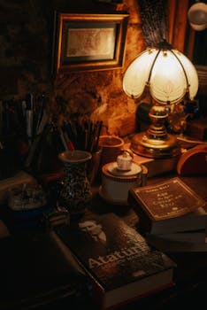 Warmly lit study desk with vintage lamp, books, and writing instruments creating a cozy atmosphere.