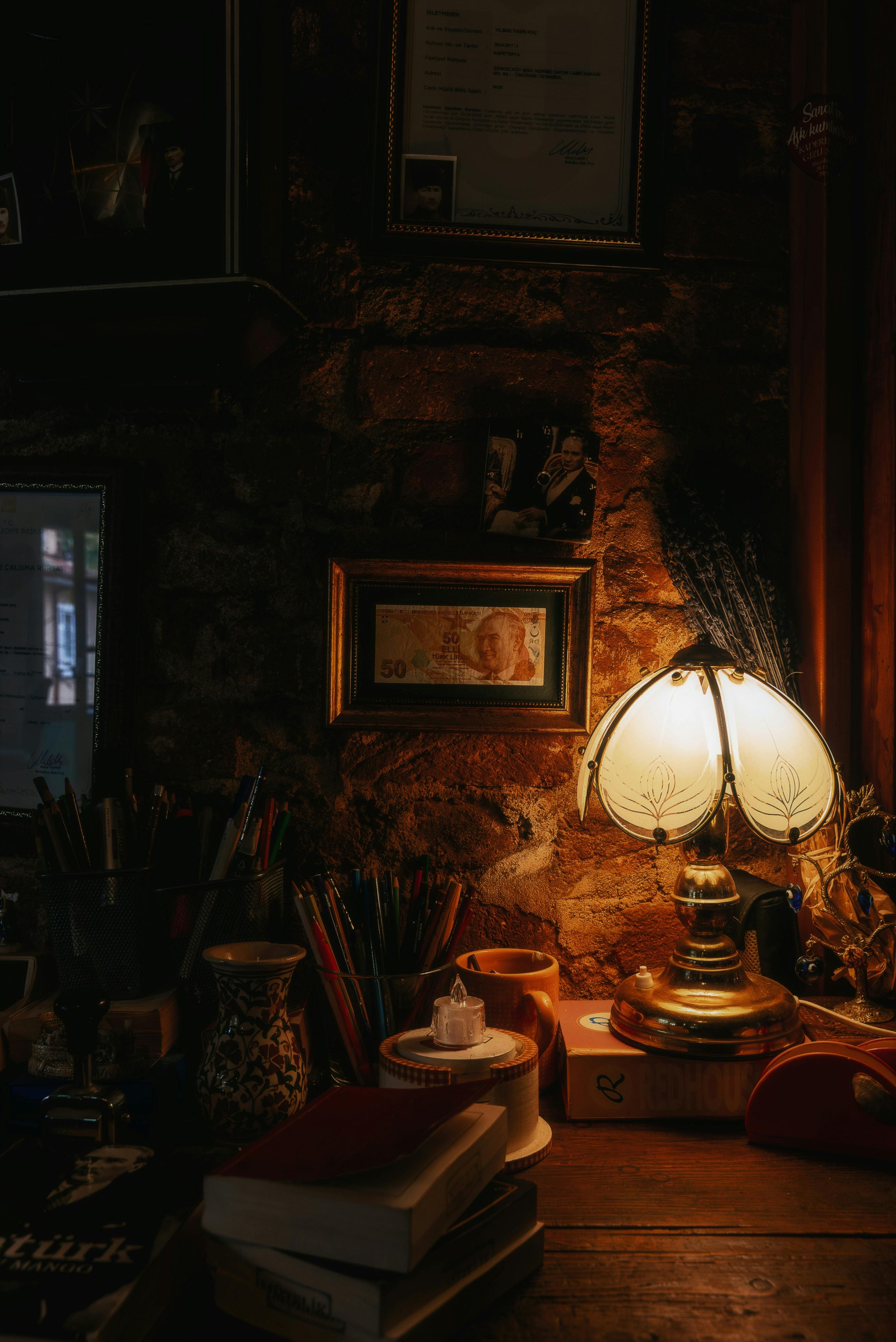 Gratis Vintage skrivebordsscene med varmt lampelys, bøger og kunstnerisk indretning i et hyggeligt arbejdsmiljø. Lagerfoto