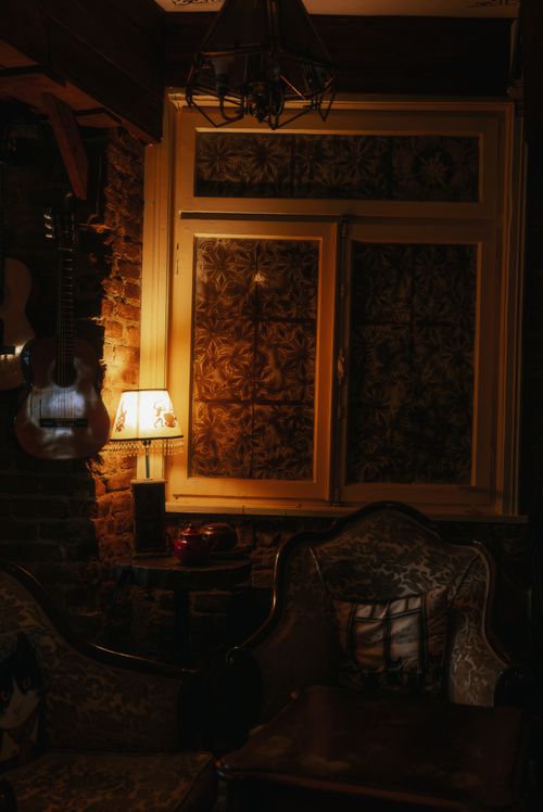 Free Warmly lit vintage living room featuring ornate windows and an acoustic guitar for a cozy ambiance. Stock Photo