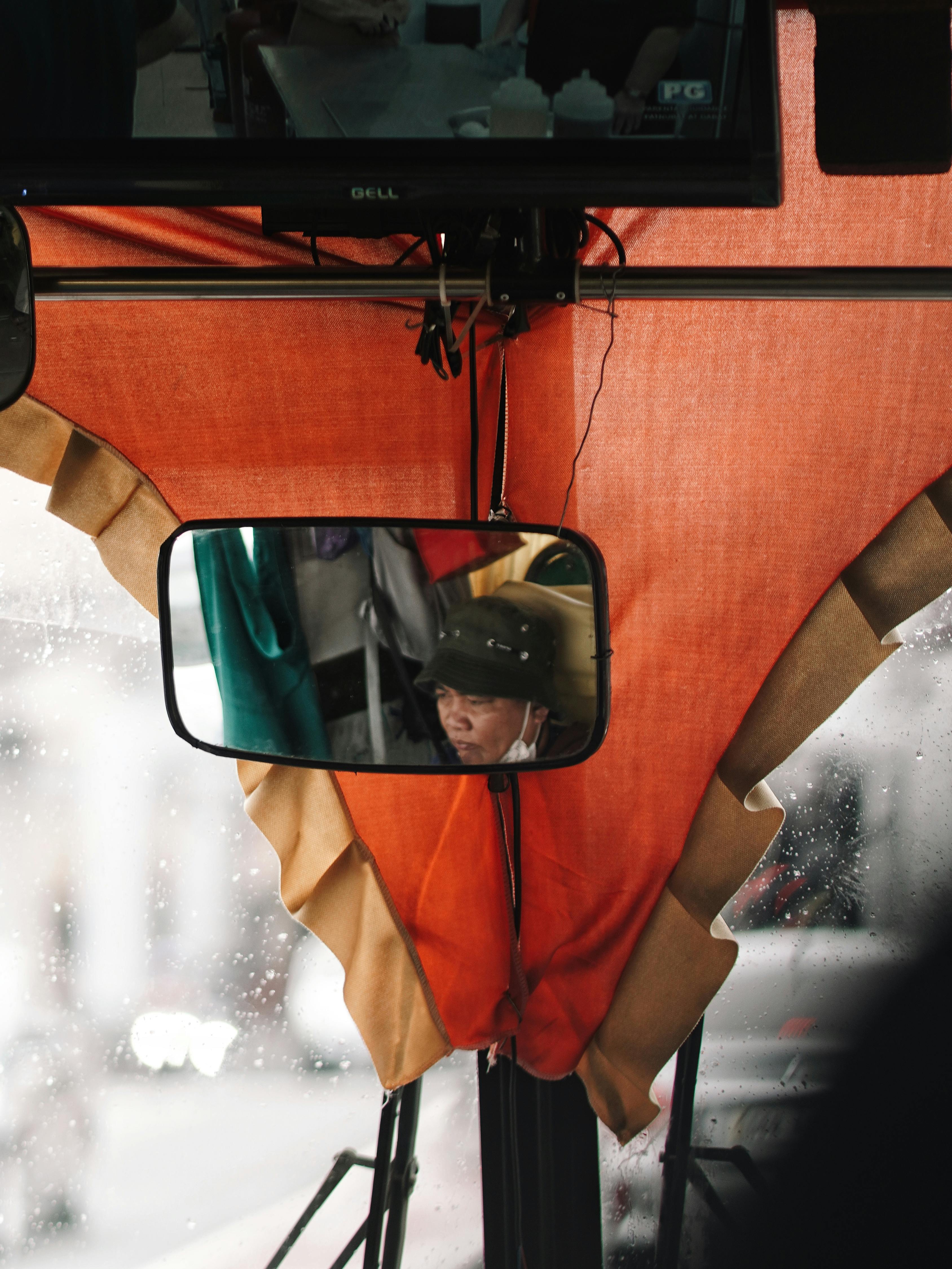 Free Bus passenger reflected in rearview mirror with orange curtains, capturing a candid travel moment. Stock Photo