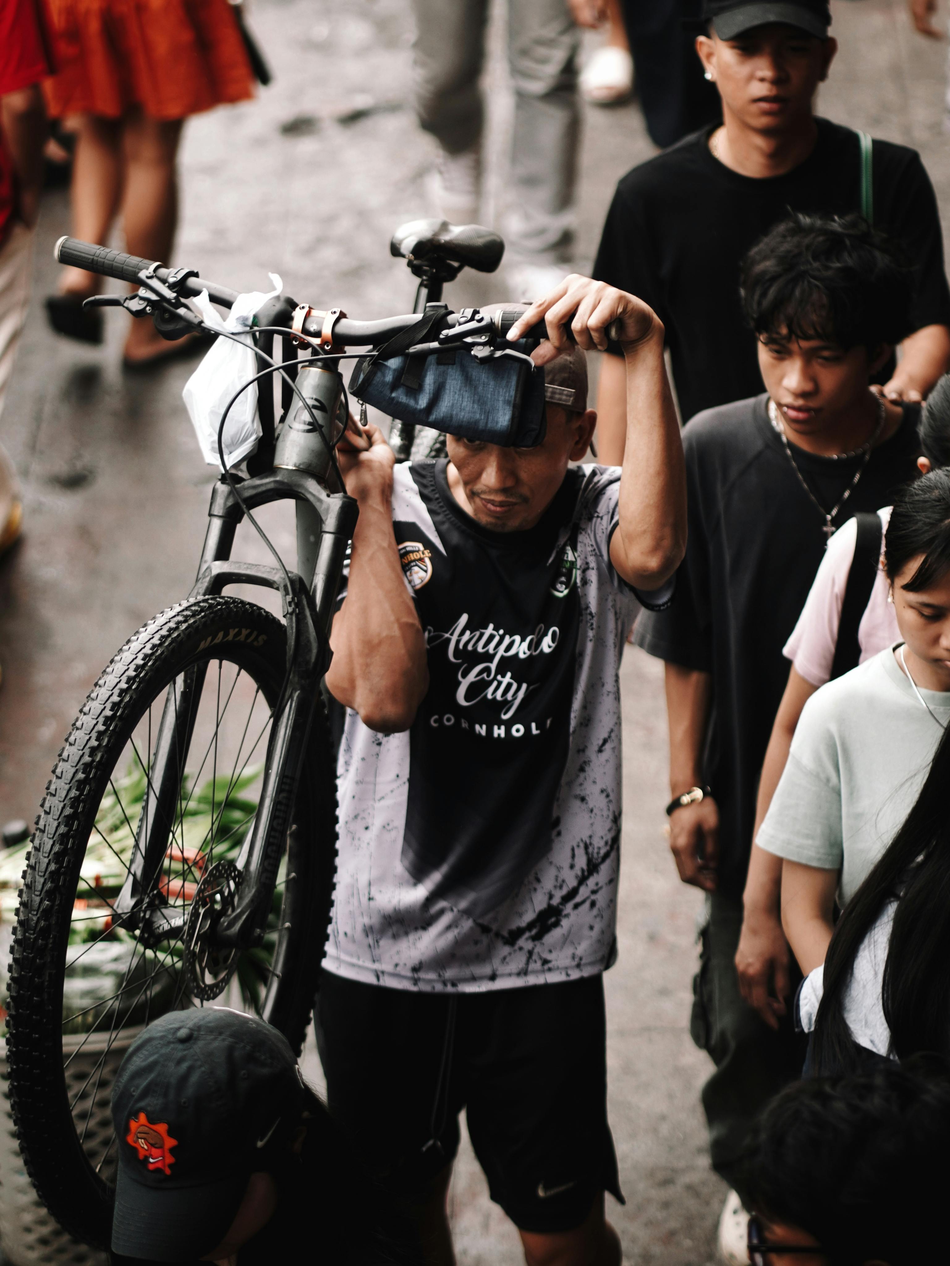 Gratis Una scena urbana movimentata con un ciclista che trasporta una bicicletta in alto in mezzo a una folla eterogenea. Foto a disposizione