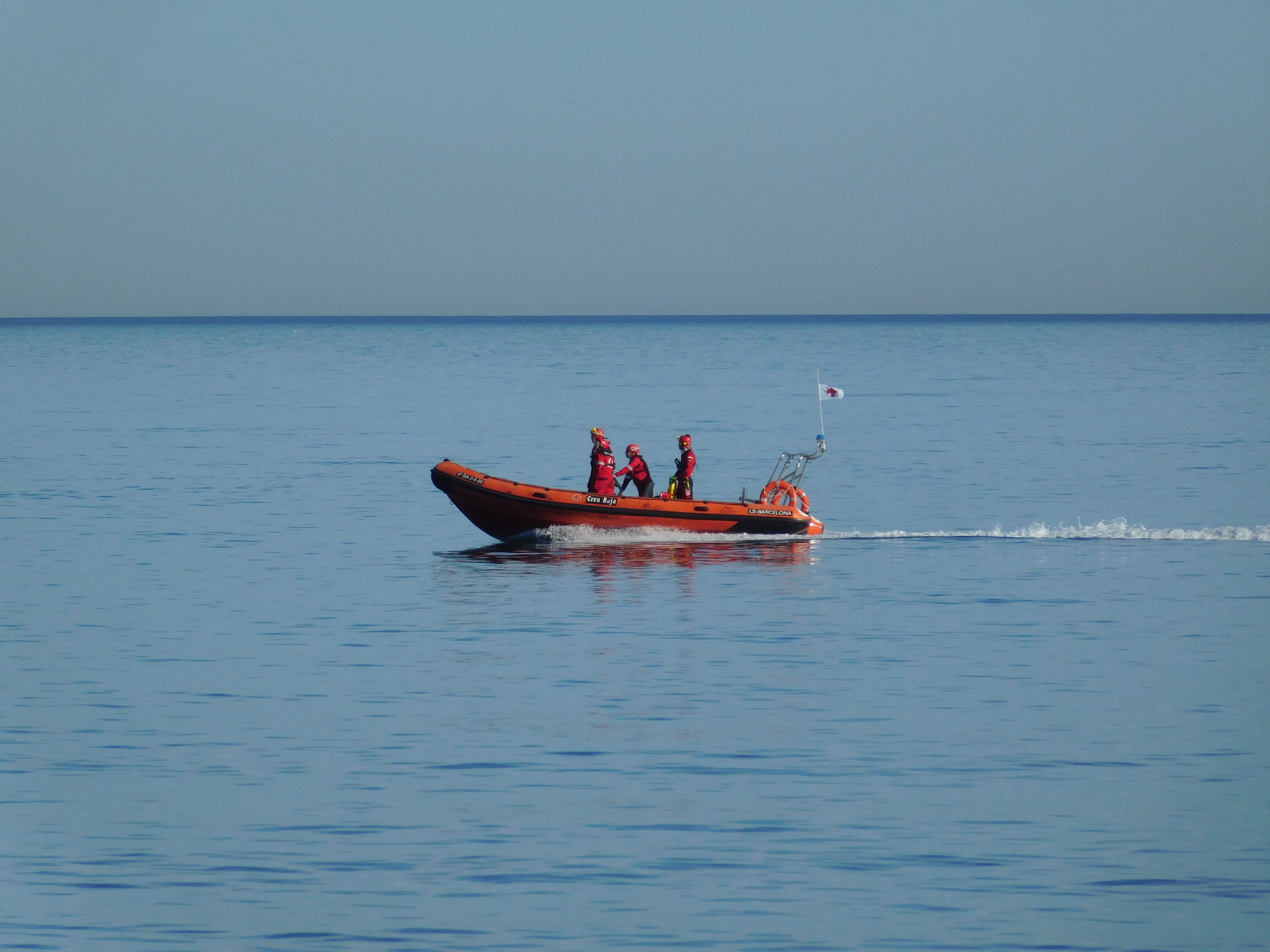 Rescue crew travel in an inflatable boat across calm sea under a clear sky
