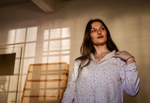 Free A woman stands confidently in a softly lit room with sunlight streaming through the window. Stock Photo