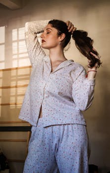 A woman stands indoors, in pajamas, bathed in soft morning light.